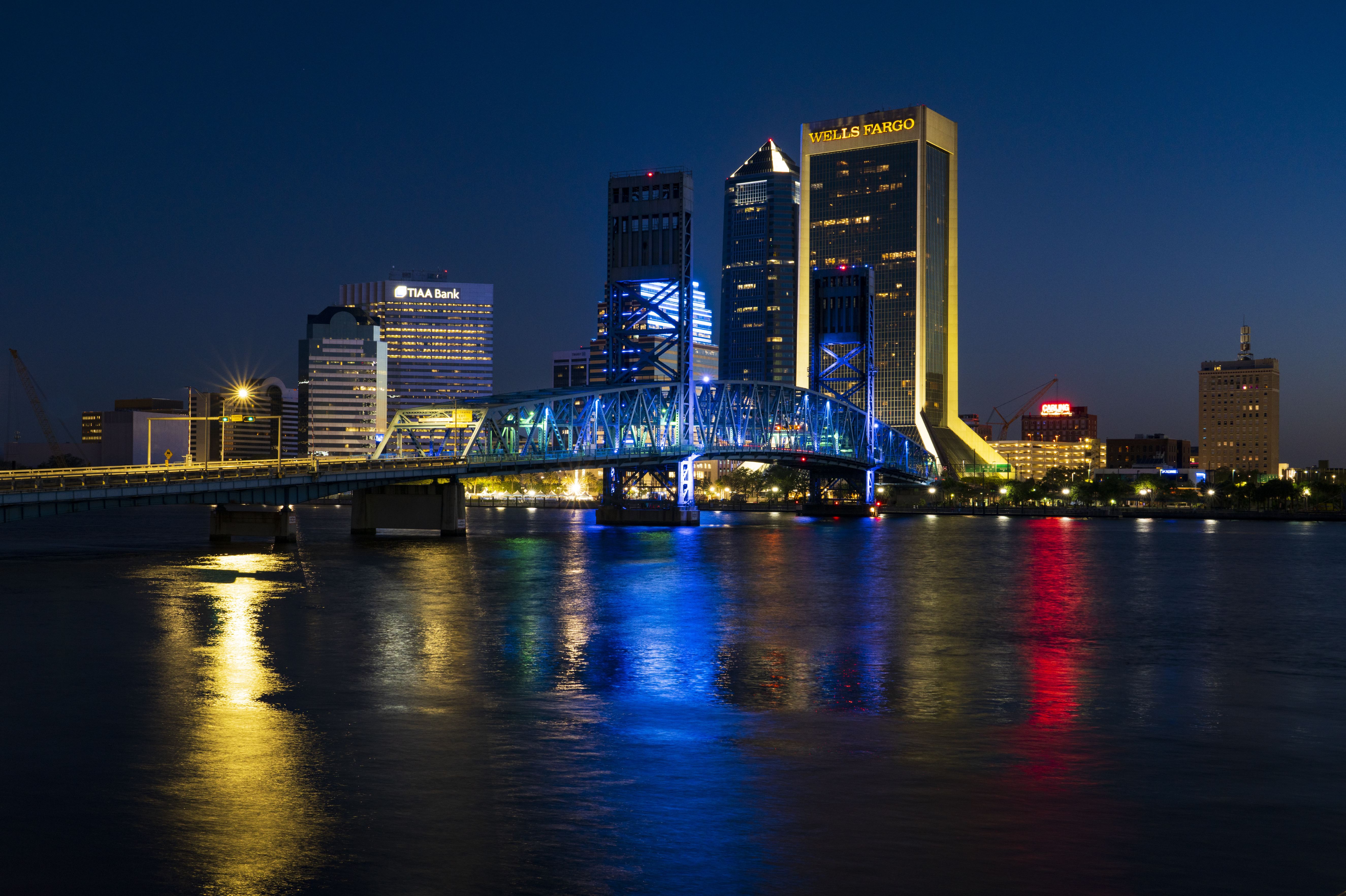 Skyline view of Jacksonville features John Alsop Bridge at night with colorful lights reflecting in water, Florida