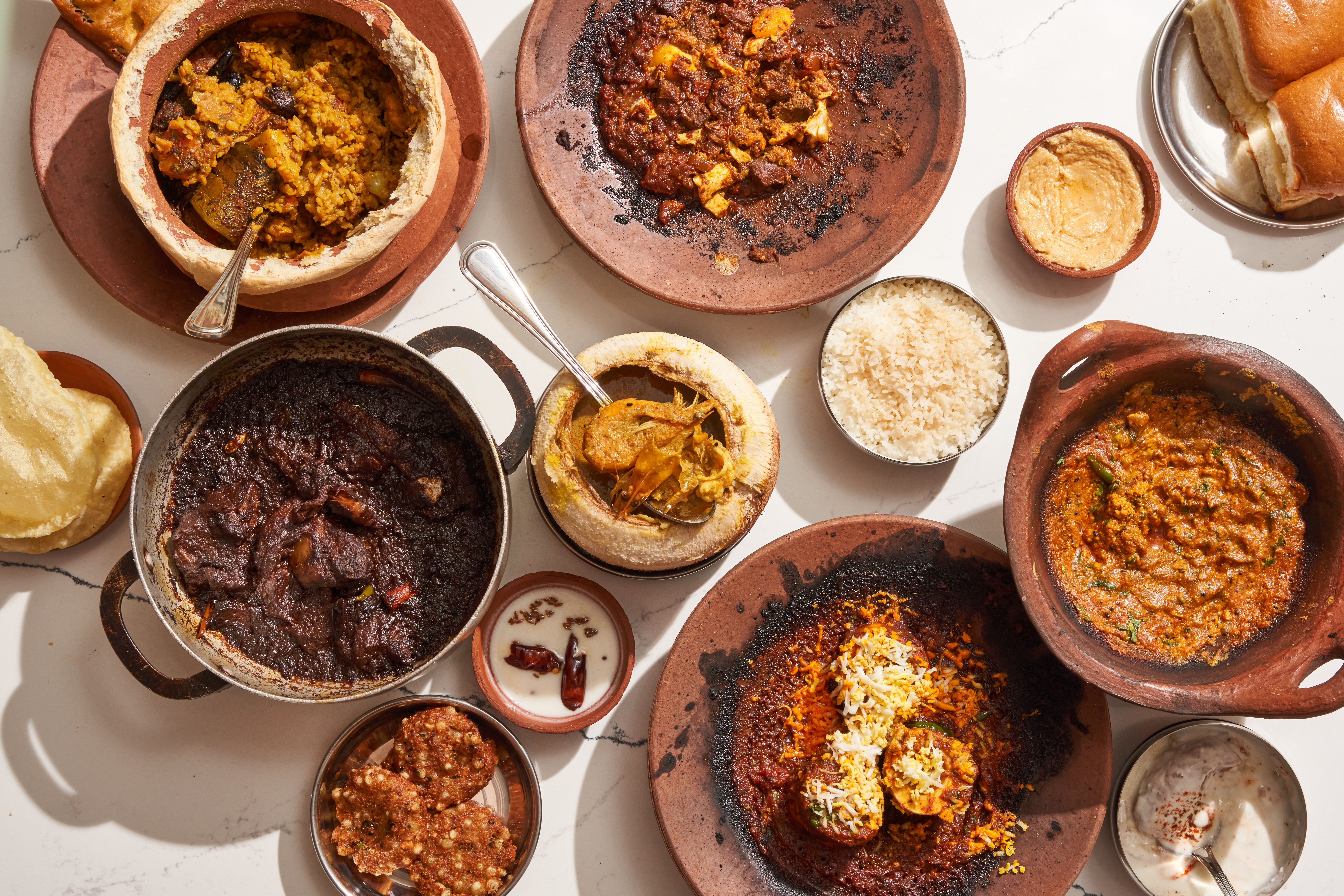 An overhead shot of food in clay pots and pans arranged on a white table.