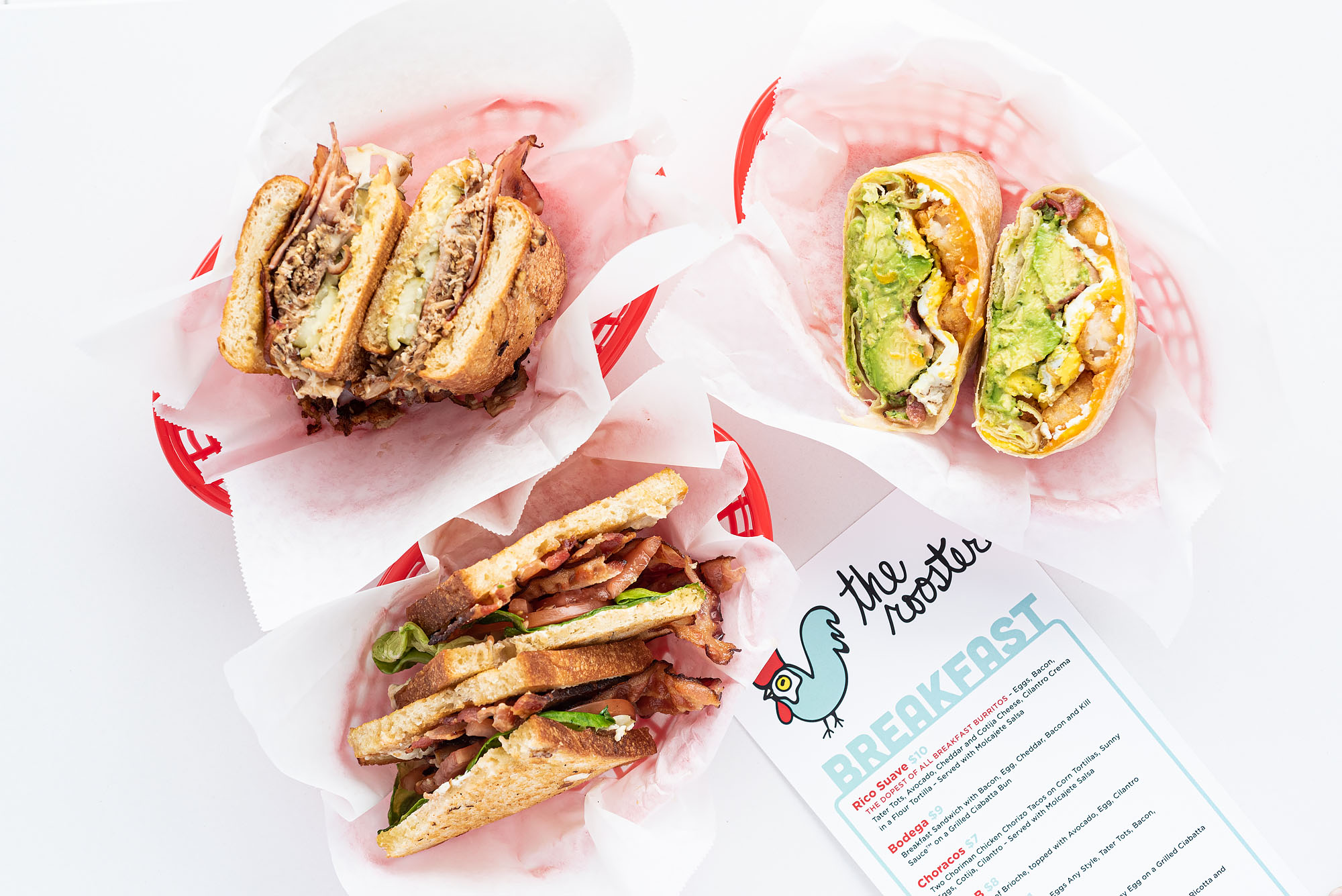 A trio of sandwiches on a bright white counter including a breakfast burrito.