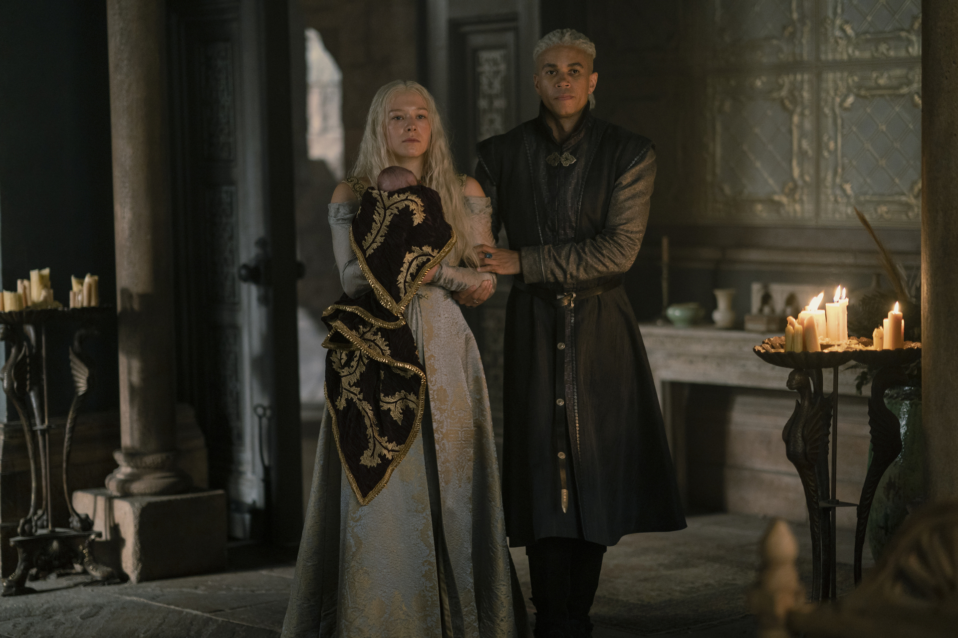 Emma D’Arcy and John MacMillan as Rhaenyra Targaryen and Ser Laenor Velaryon, respectively, standing in their chambers in House of the Dragon, with Rhaenyra holding a baby