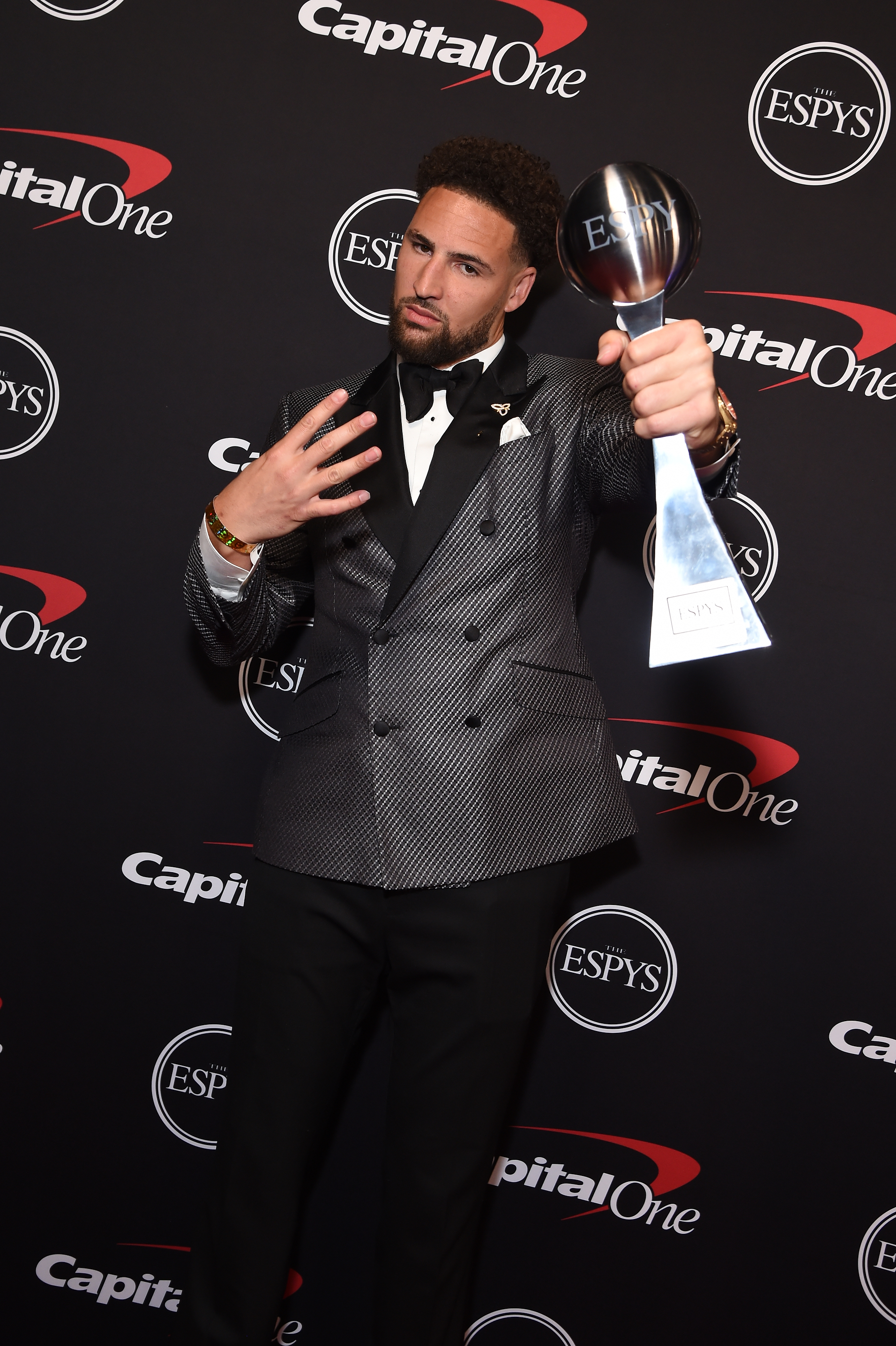 Klay Thompson holding the Larry O’Brien trophy and flashing four fingers while in a suit at the ESPYs 
