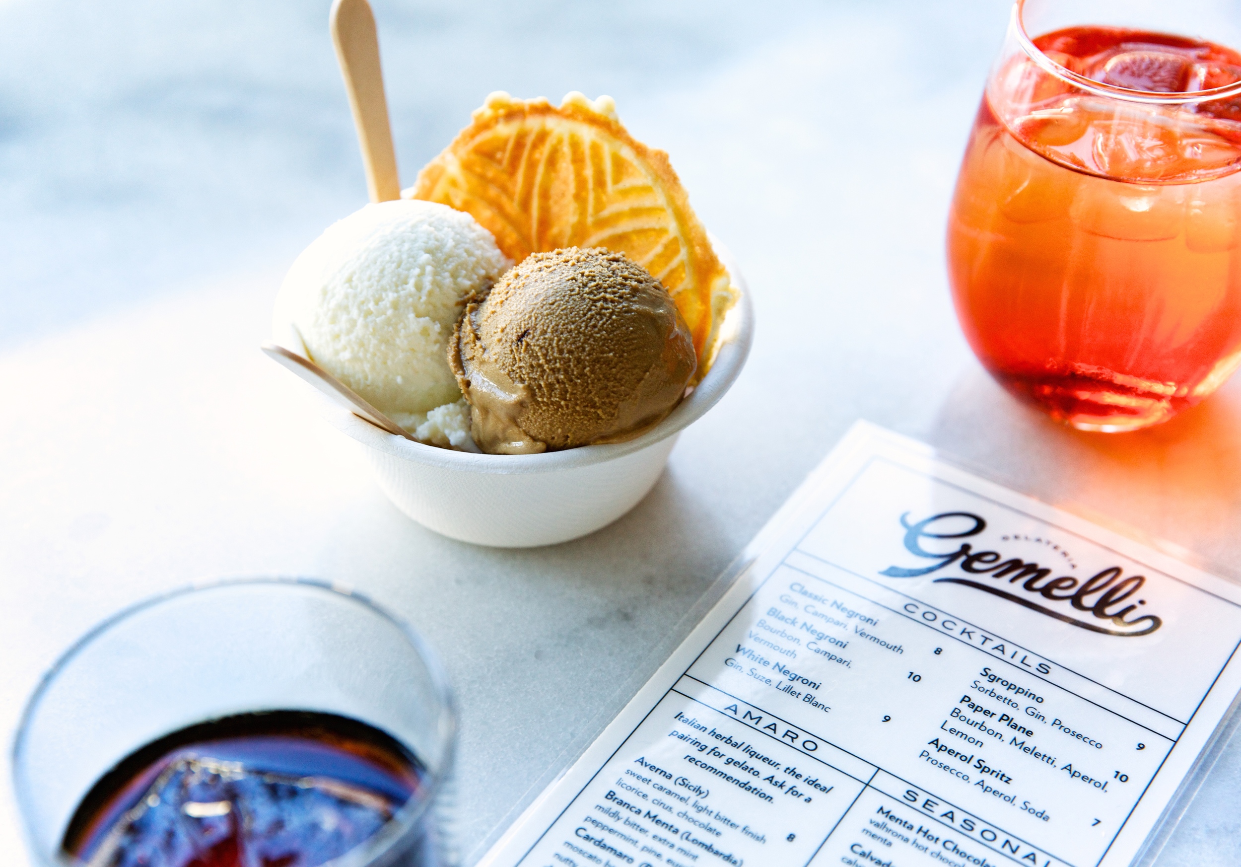 A small bowl of a vanilla and chocolate ice cream scoops with a cookie next to an orange cocktail.