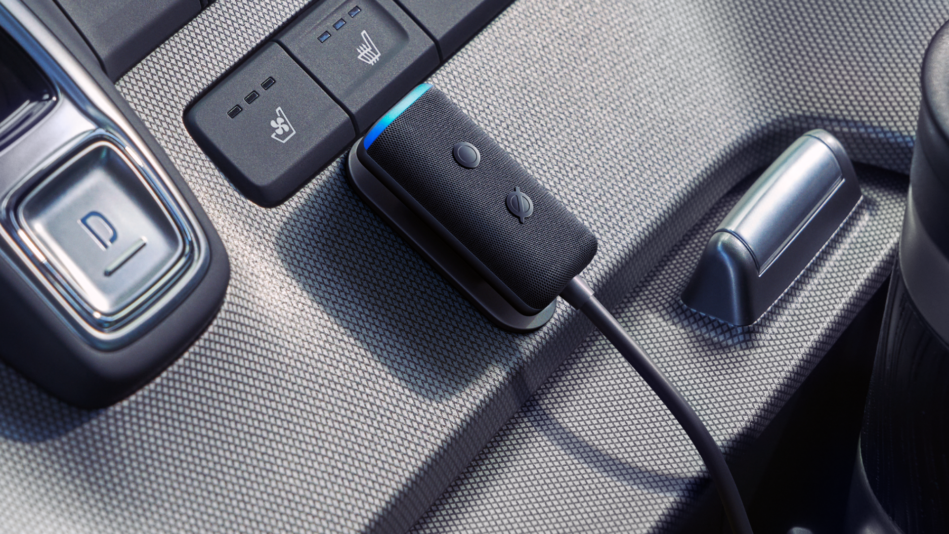An Amazon Echo Auto mounted to the center console of a car, just below buttons for seat heater controls.