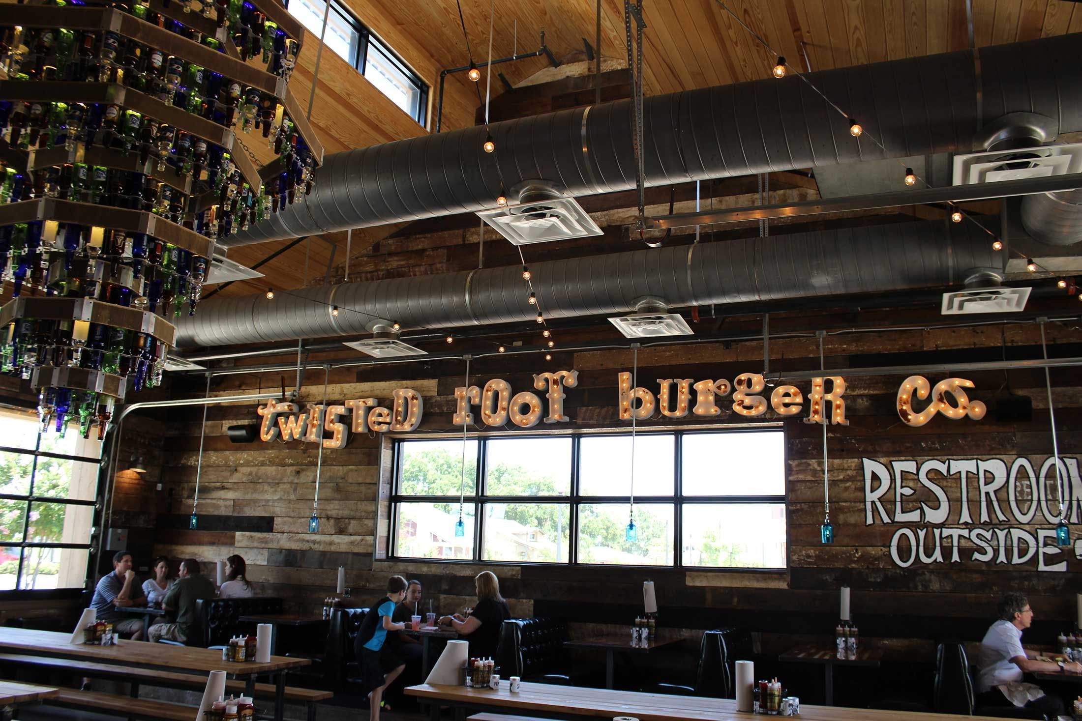 The interior of a restaurant with an exposed ceiling, walls lined with rough wood, and an all lower caps sign reading “twisted root burger co.”
