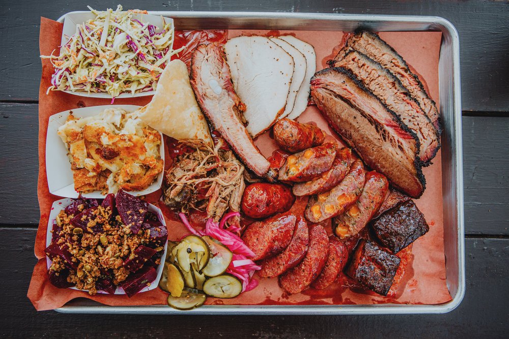 A tray of barbecue meats, sides, pickles, and bread.