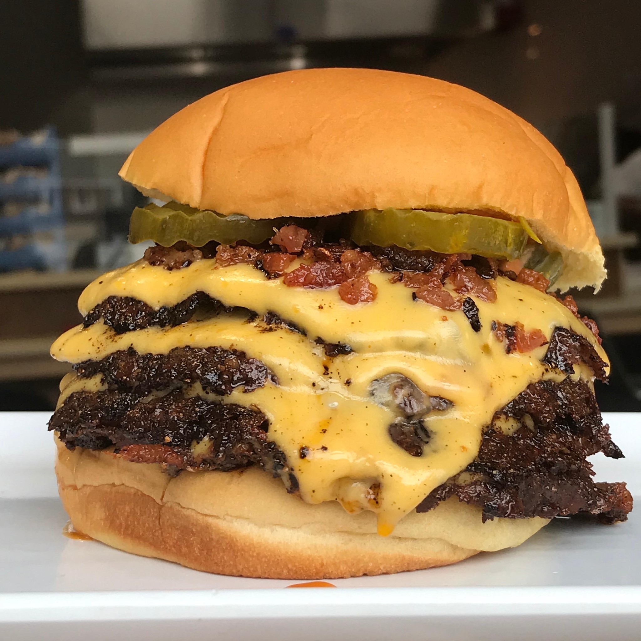 A triple cheese burger with bacon bits and dill pickles