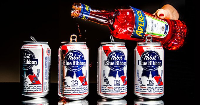 four Pabst Blue Ribbon beer cans and a bottle of Aperol held aloft as if to be poured into the cans