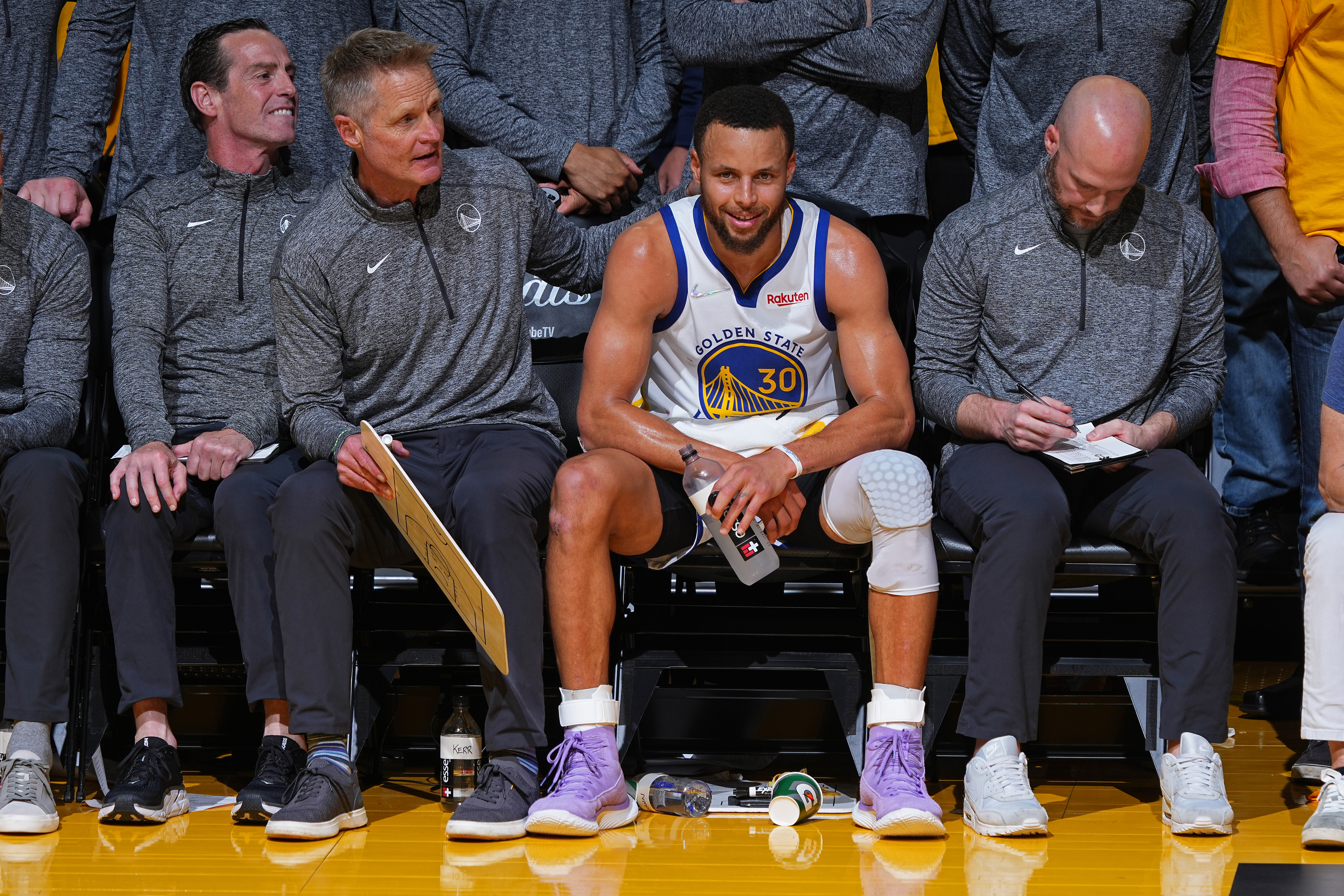 Steph Curry sitting on the bench between coaches