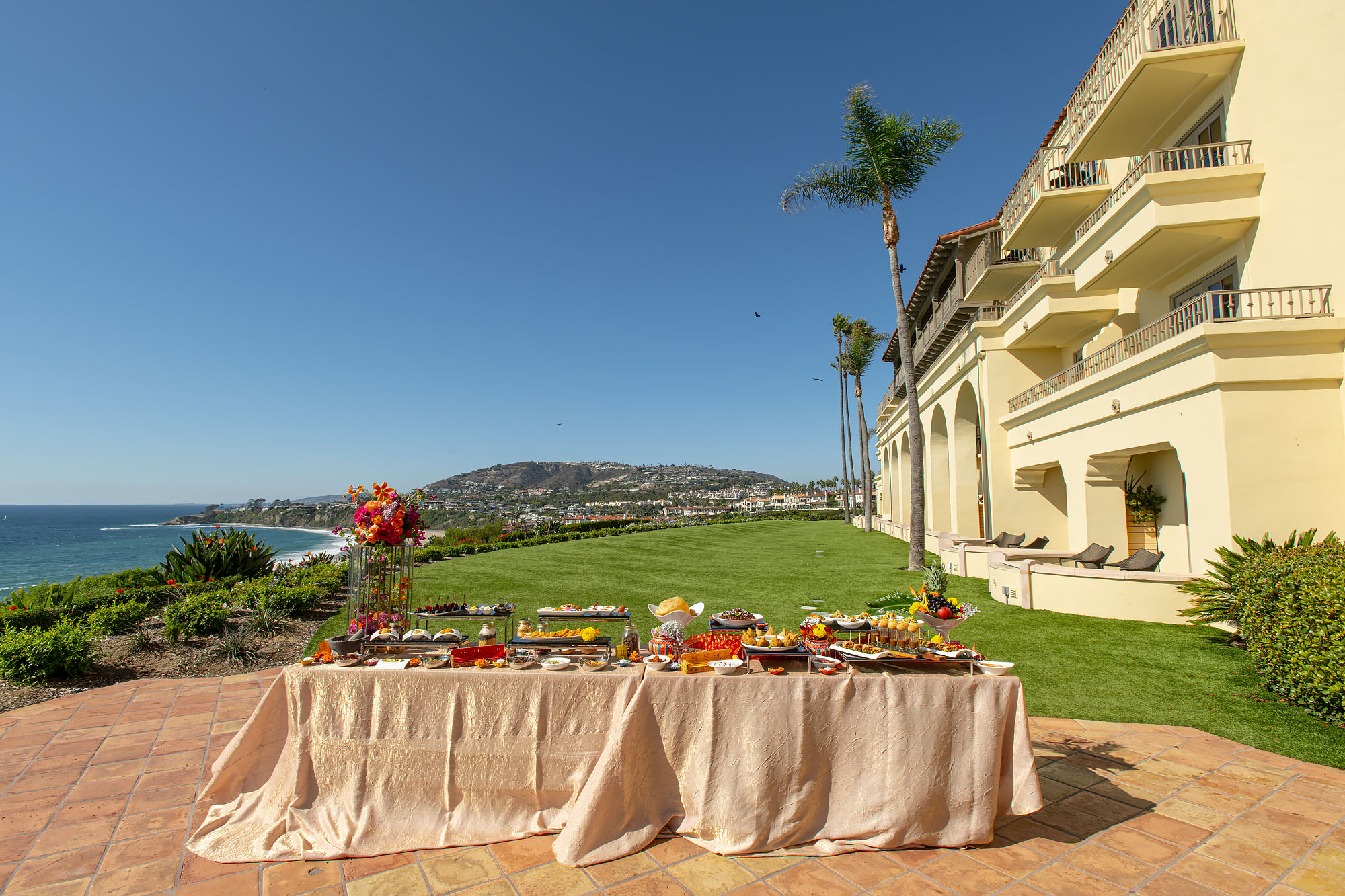 Landscape view of a hotel lawn overlooking the Pacific Ocean with a wedding buffet table spread in the foreground.