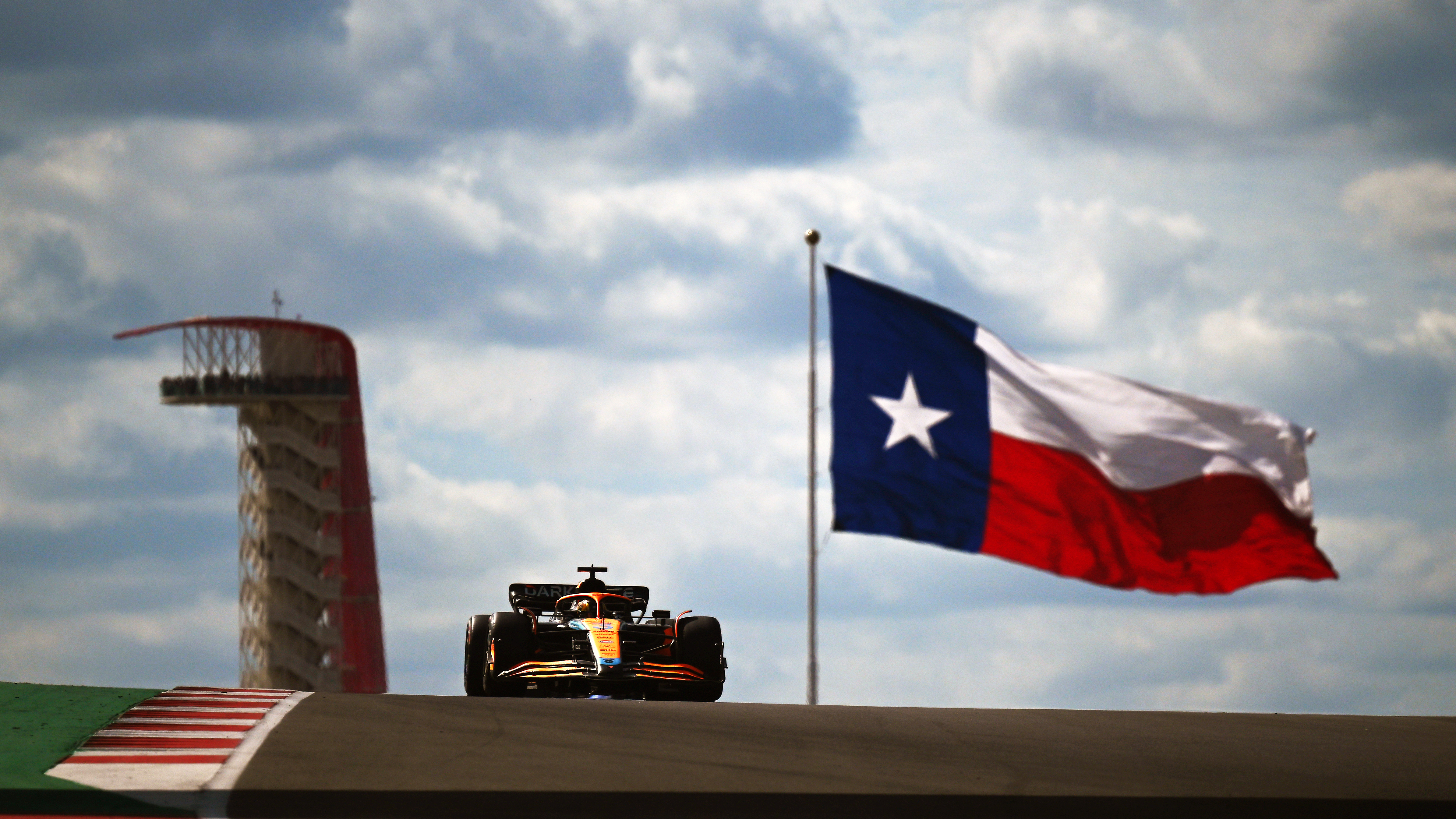 A car on a race track in front of a giant Texas flag.