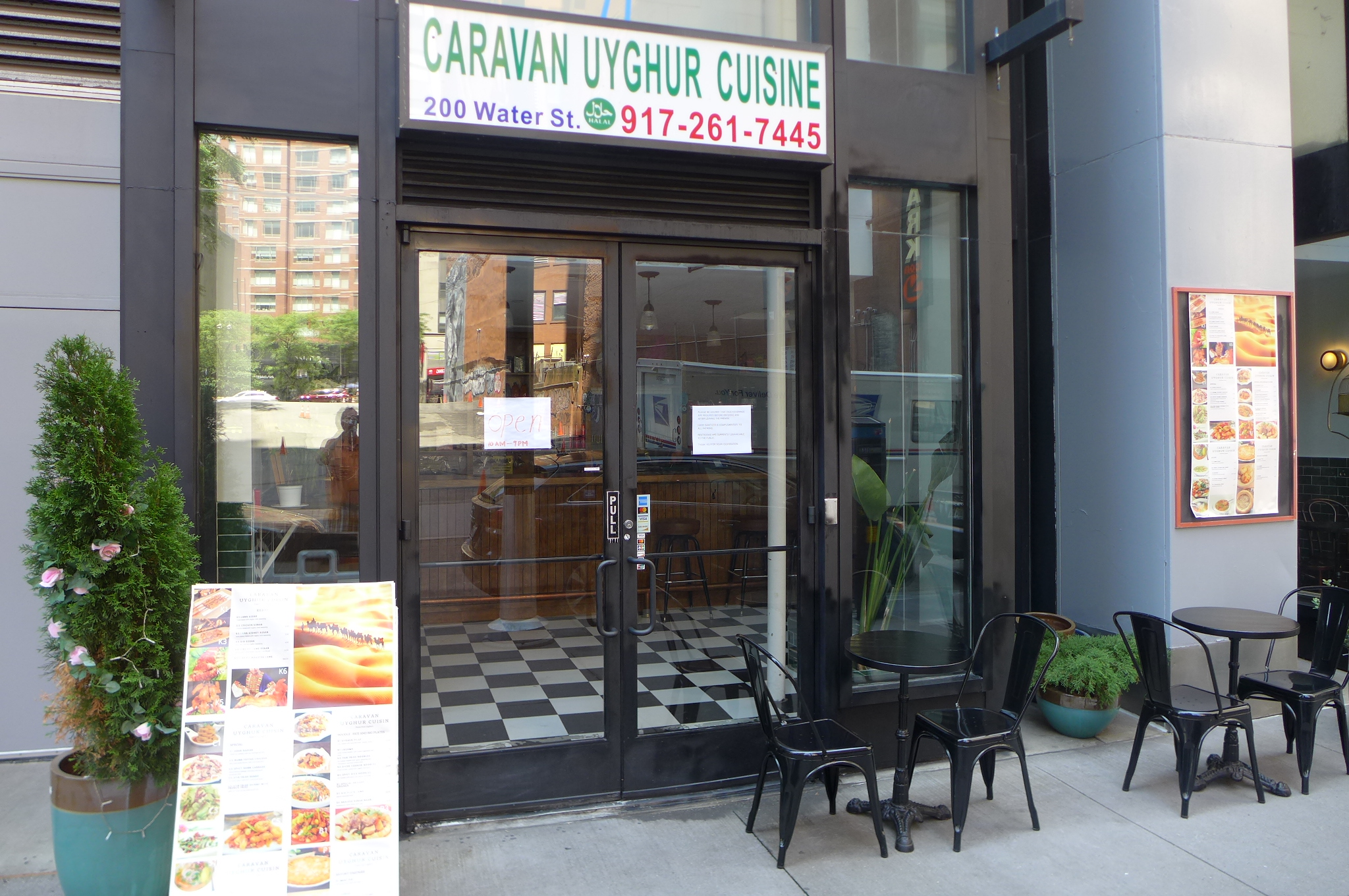 A blue sign above a black metal door with a propped up giant menu on the left side.