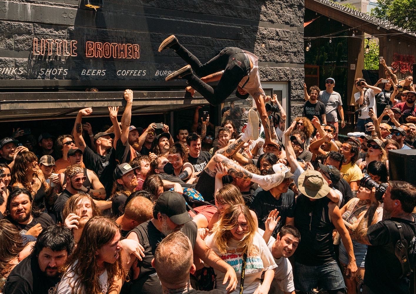 A crowd of people at a concert outside with someone crowdsurfing.