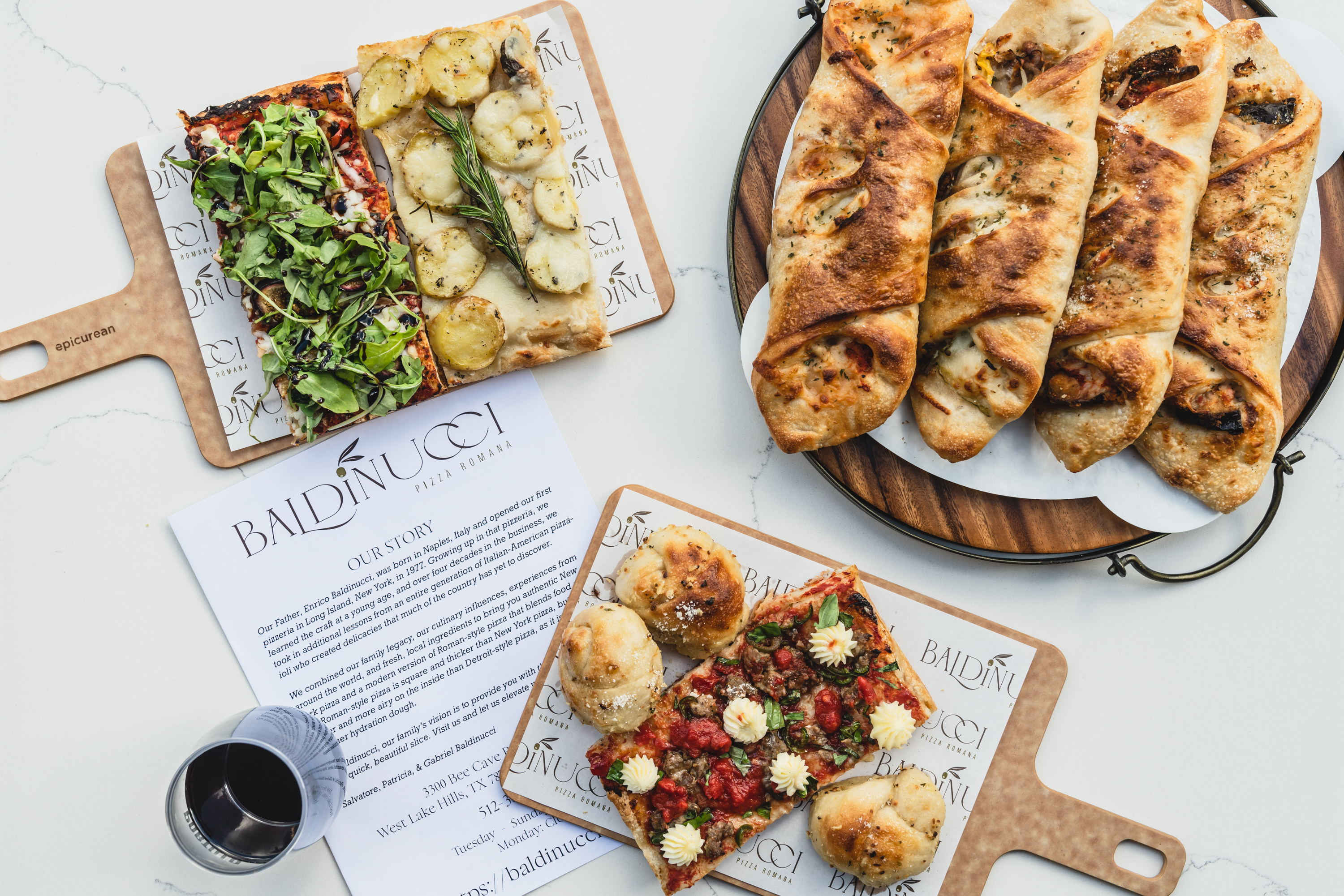 Wooden boards with two kinds of thin-crust pizza, rolled involtini, and a piece of pizza with garlic knots, with the baldinucci menu in the middle and a glass of water