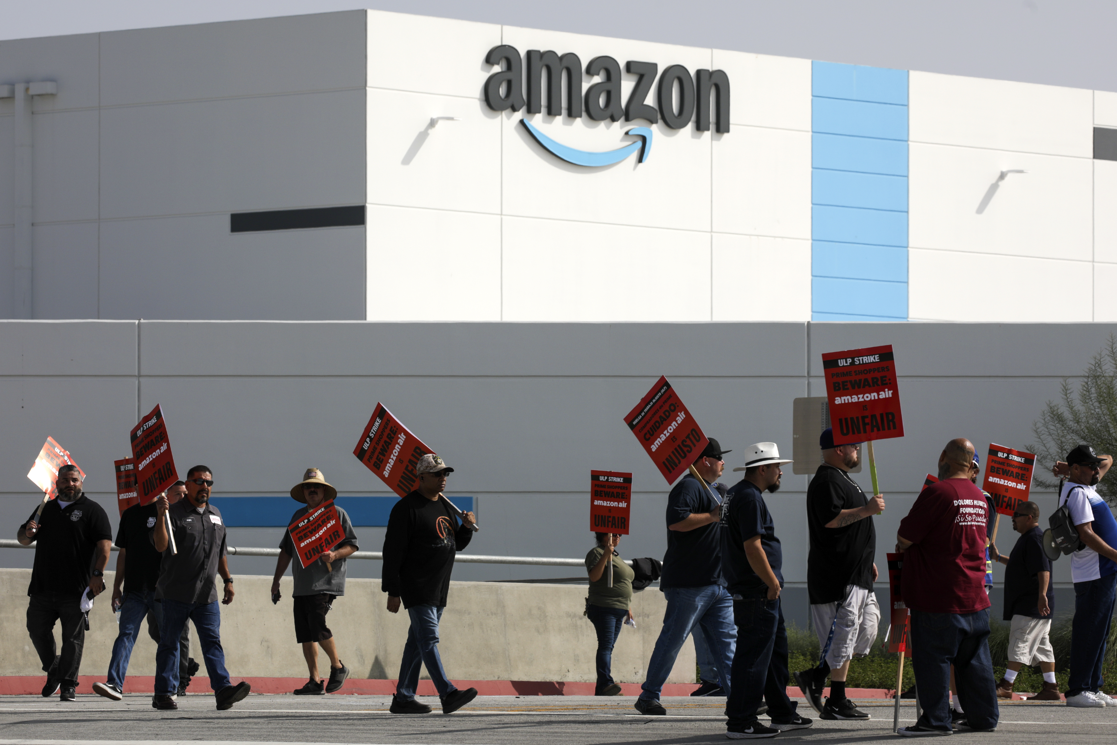 Amazon warehouse workers carrying protest signs outside a building bearing the Amazon logo.