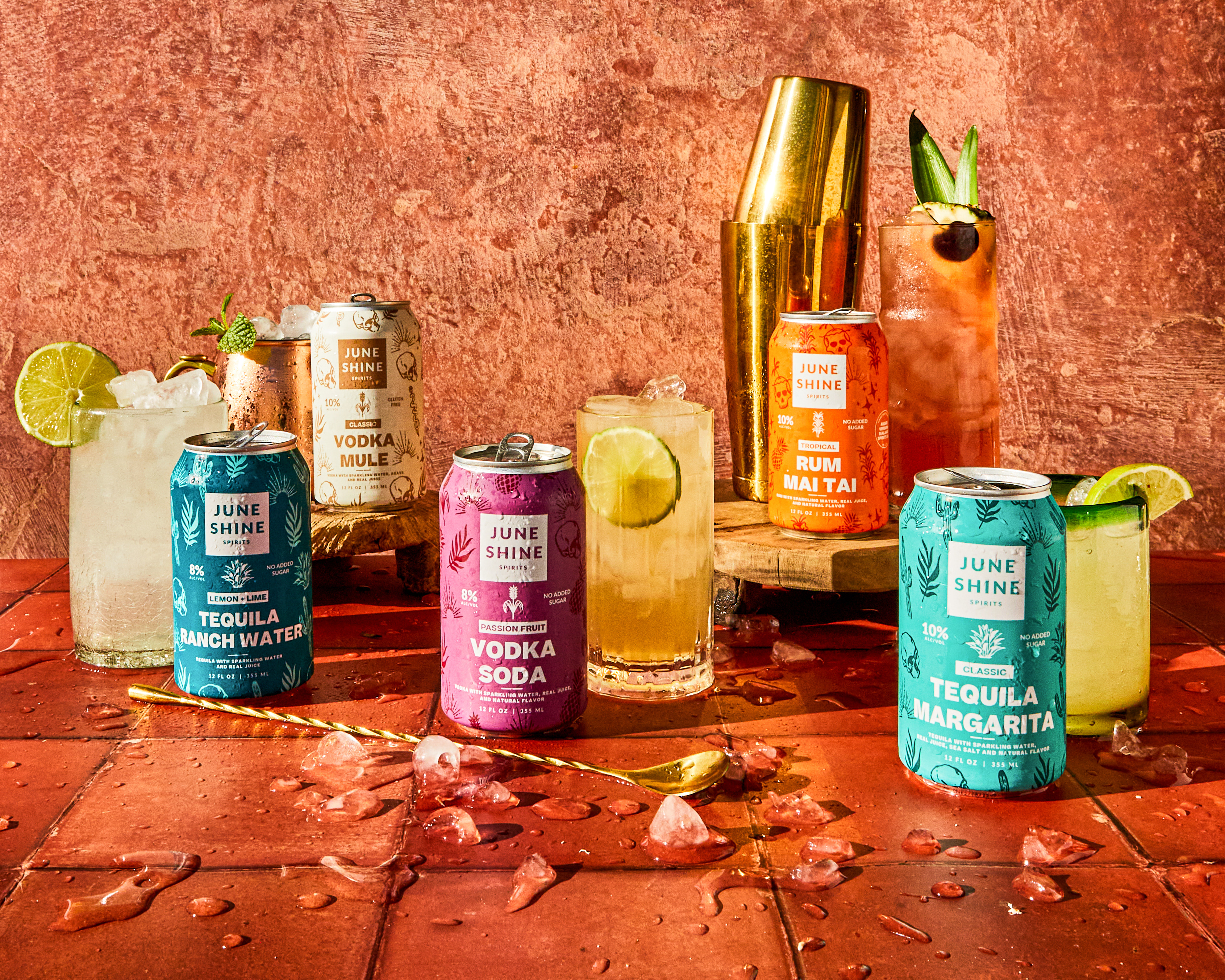 A selection of canned cocktails with lime wedges sit on terracotta tiling.