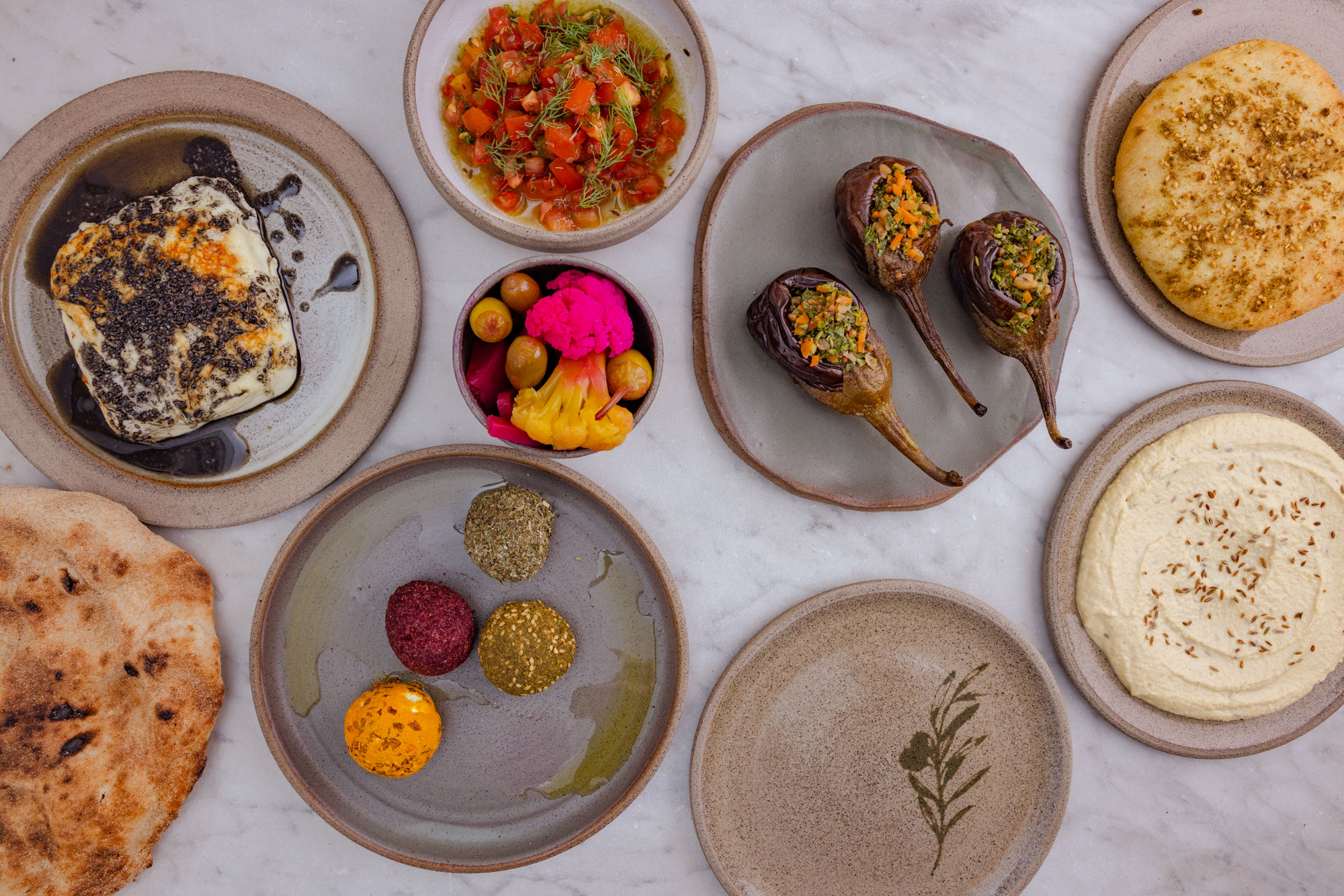 A birdseye view of pickles, breads, aubergines, tomatoes, cheese, and lentil balls on Palestinian ceramics.