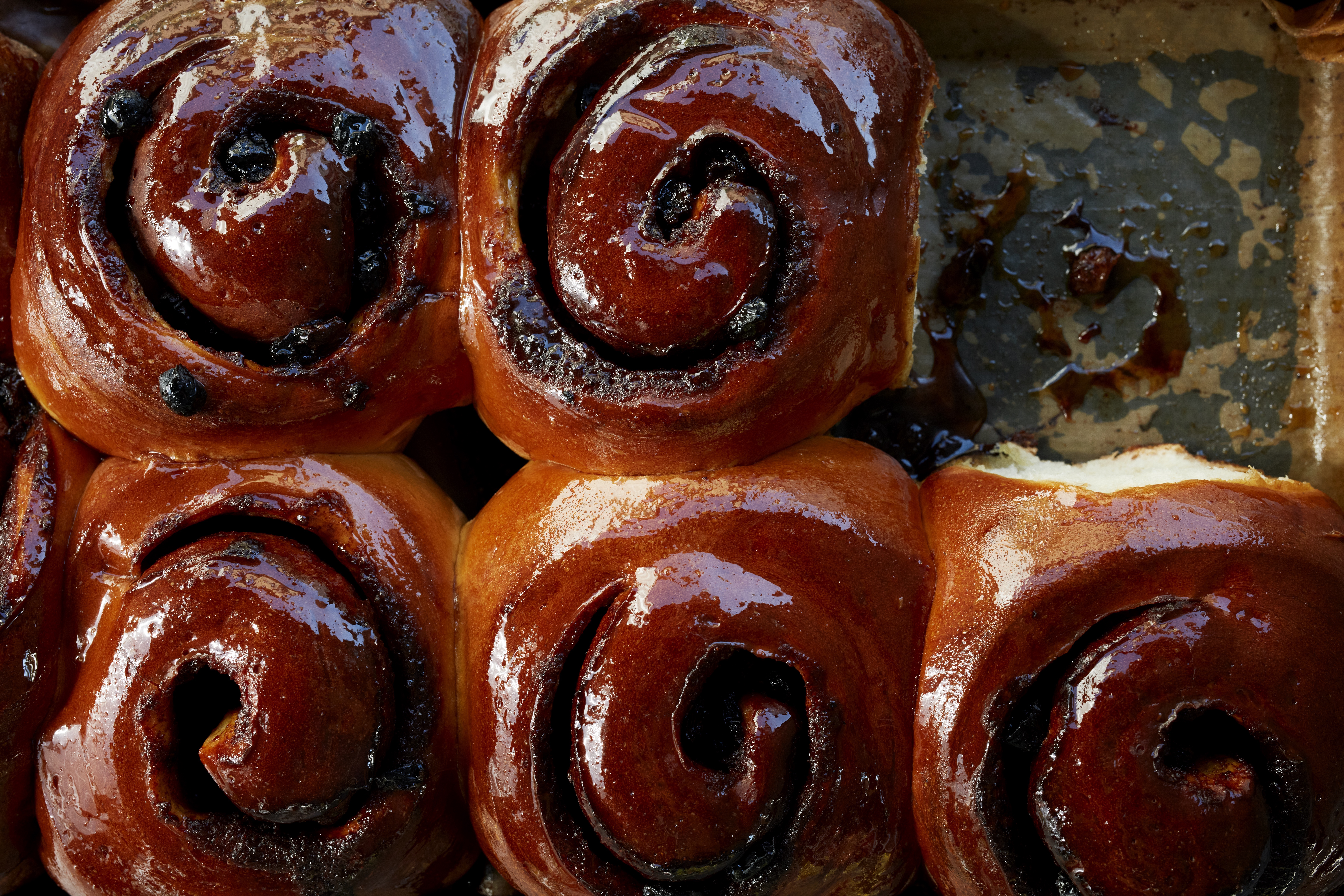 An overhead photo of five swirly glazed sticky buns with one in the top right corner removed.