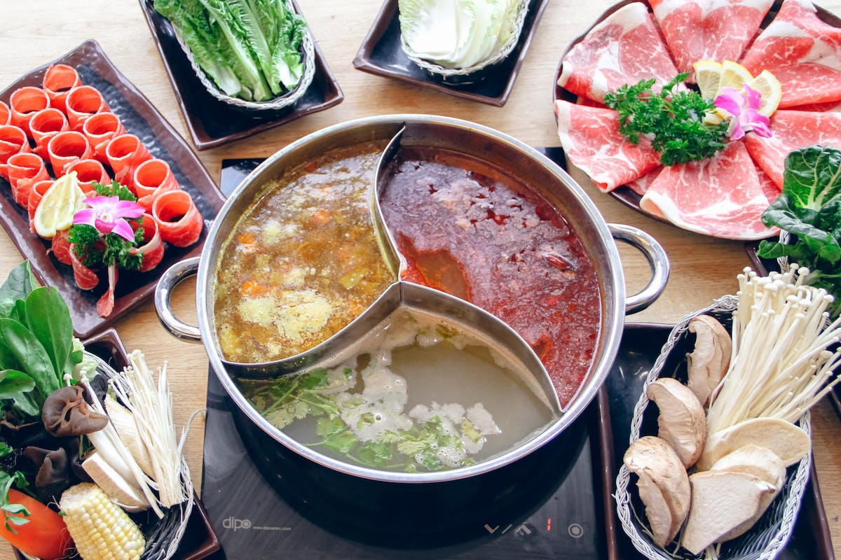 A spread of foods including a bowl in the center with three separate sections containing three distinct broths plus several plates covered in meats and vegetables destined to be cooked in the shabu-shabu hot pot.