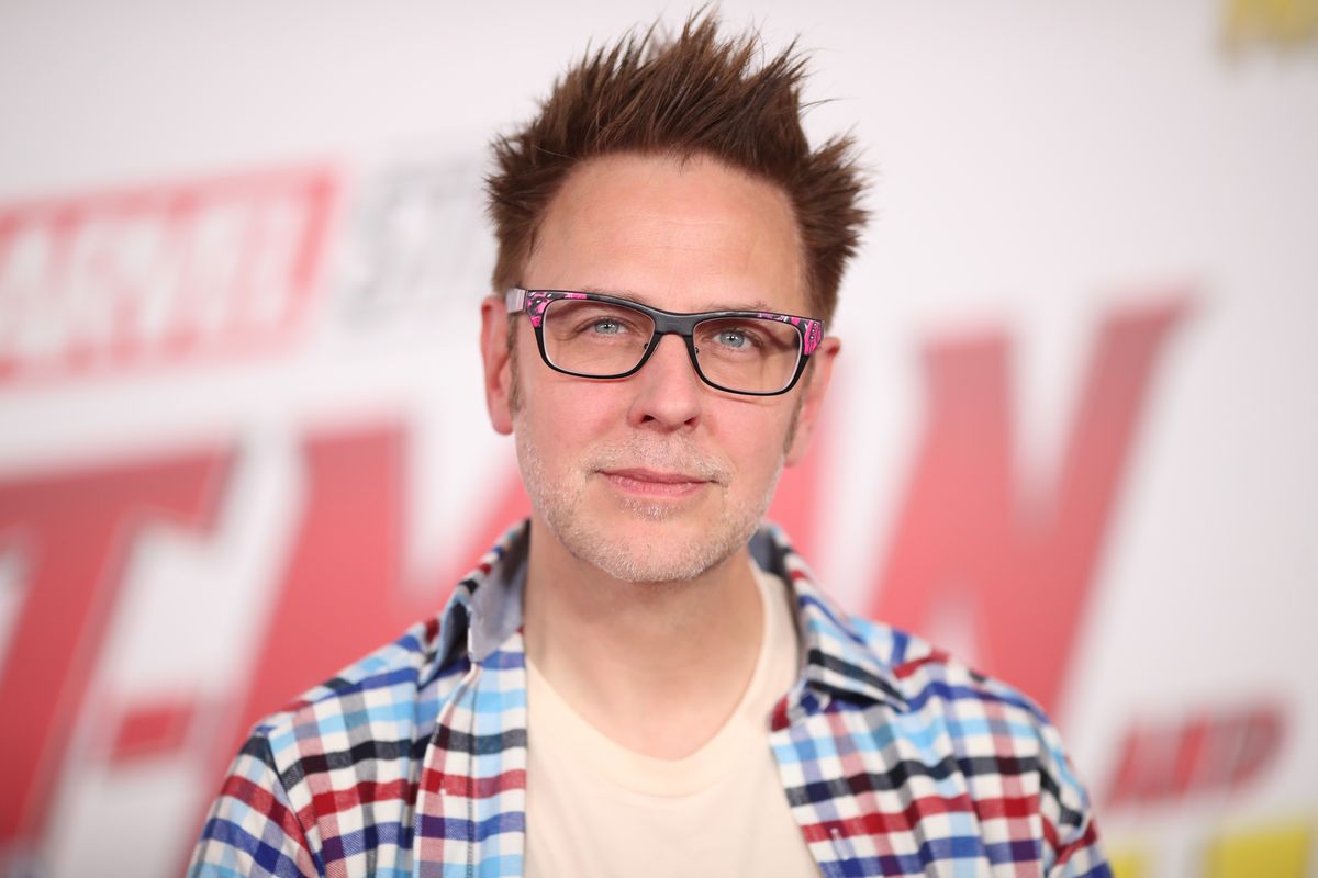 James Gunn wears glasses and a plaid shirt at a Marvel press event, with an Ant-Man logo behind him.