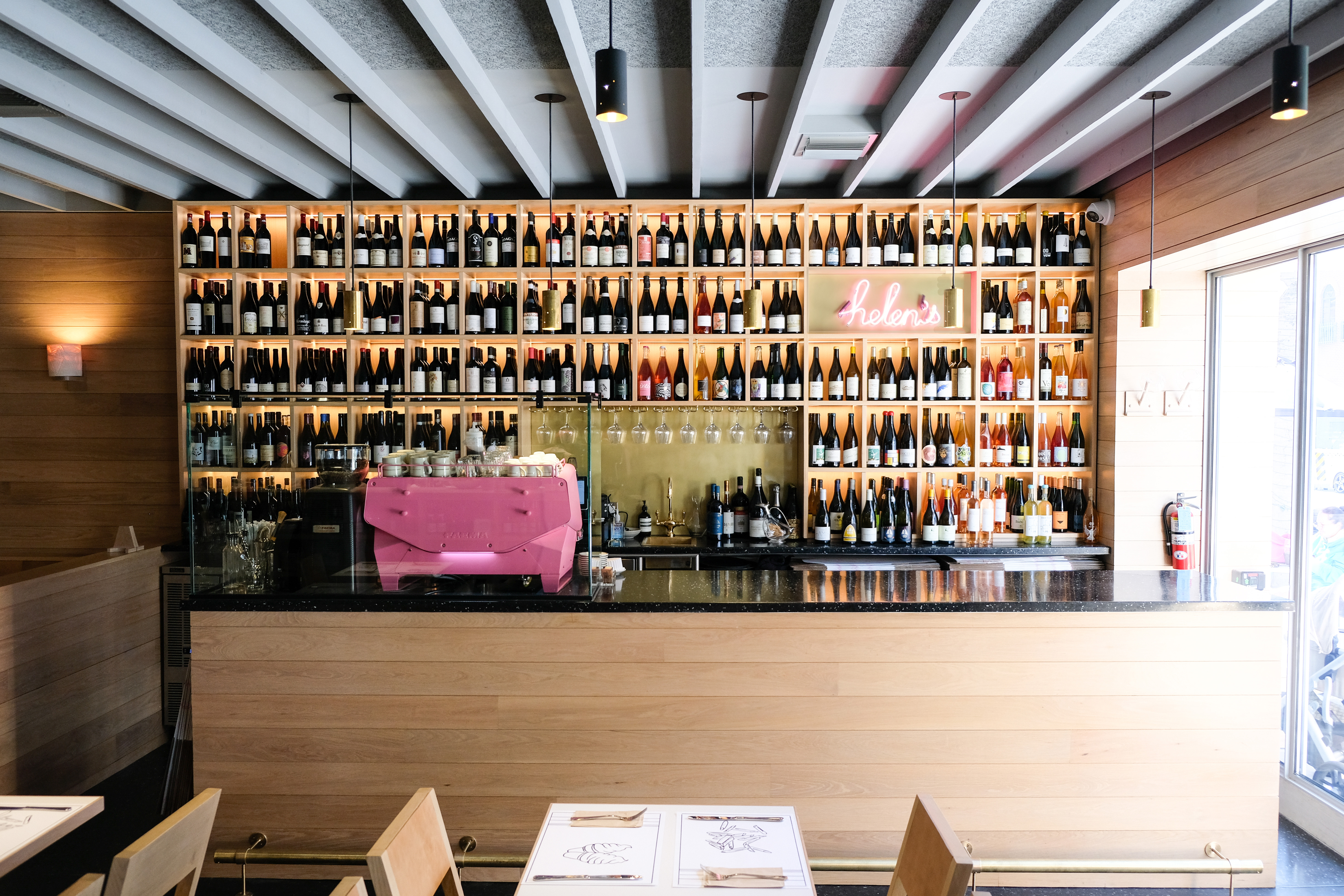 A light wooden bar with rows of wine bottles behind it.