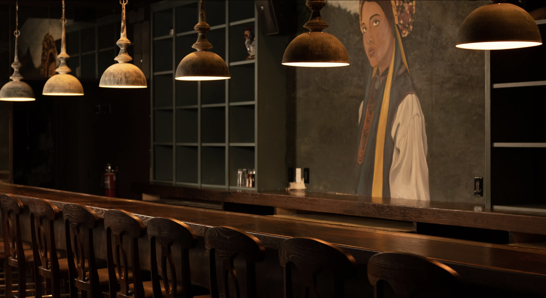 A dark bar with a mural of a woman and hanging lamps.