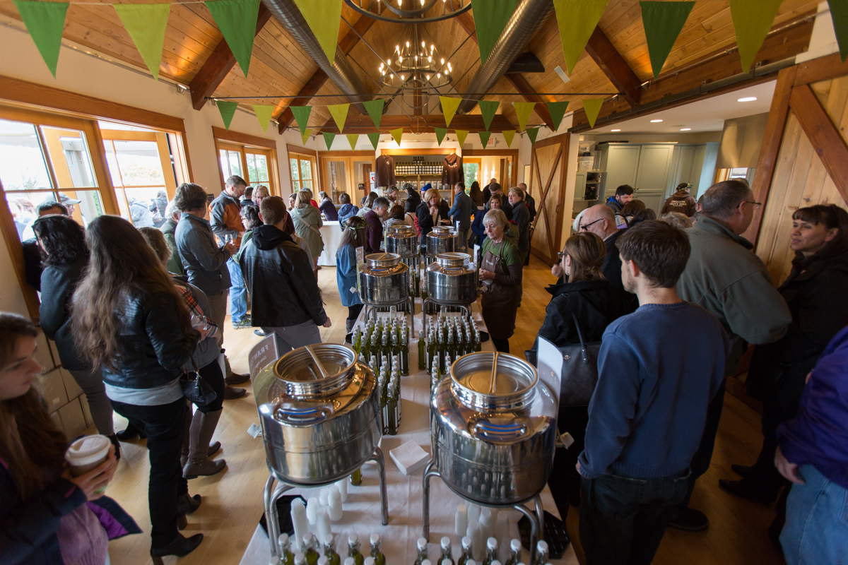 People surround a table filled with large containers and small bottles of olive oil.