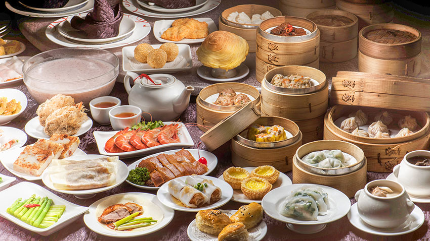 A spread of dim sum dishes and bamboo steamers are arranged on a table.