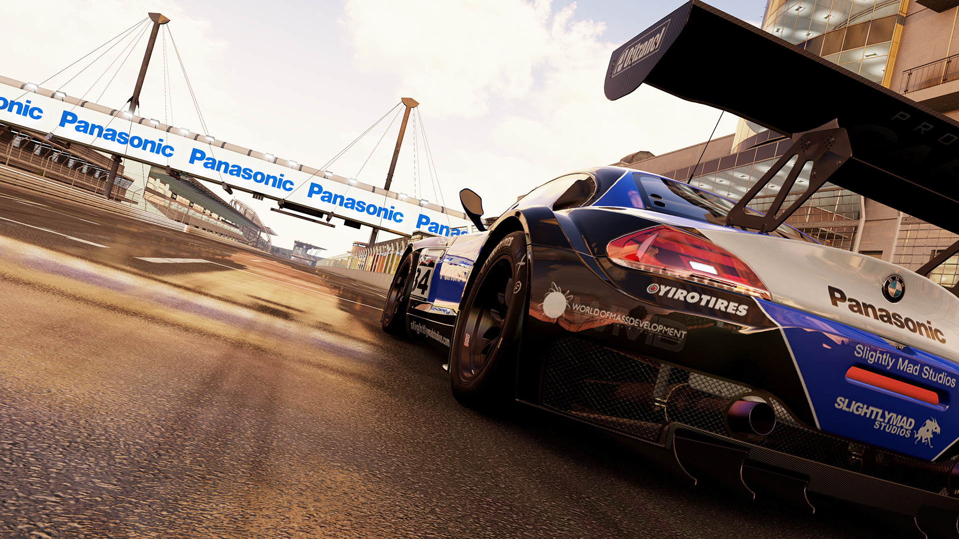 An in-game, close-up view of a tuned up street racing car with a very large spoiler, seen from the rear driver’s side bumper
