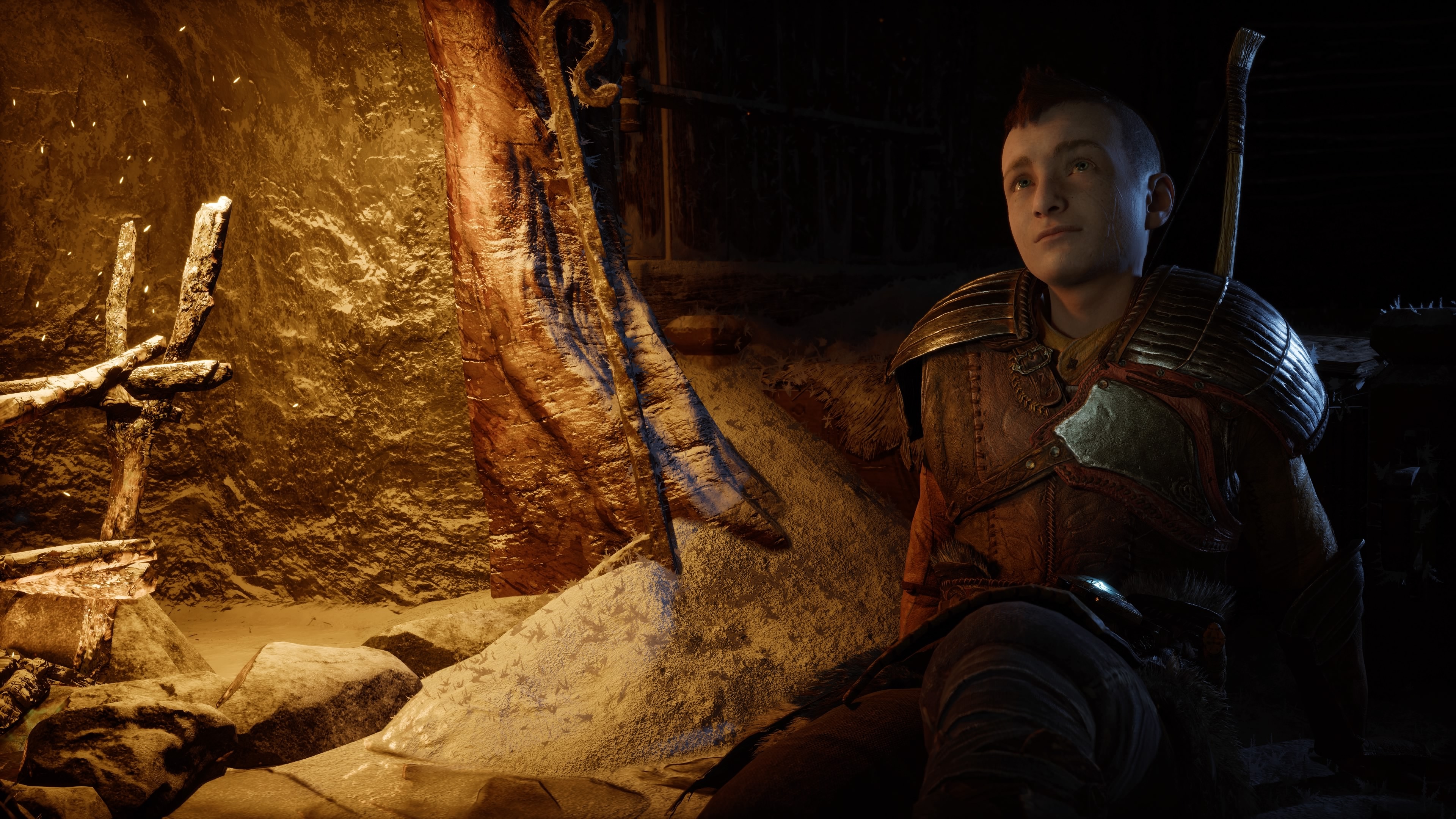 Atreus sits by a fireside looking thoughtful in God of War Ragnarök