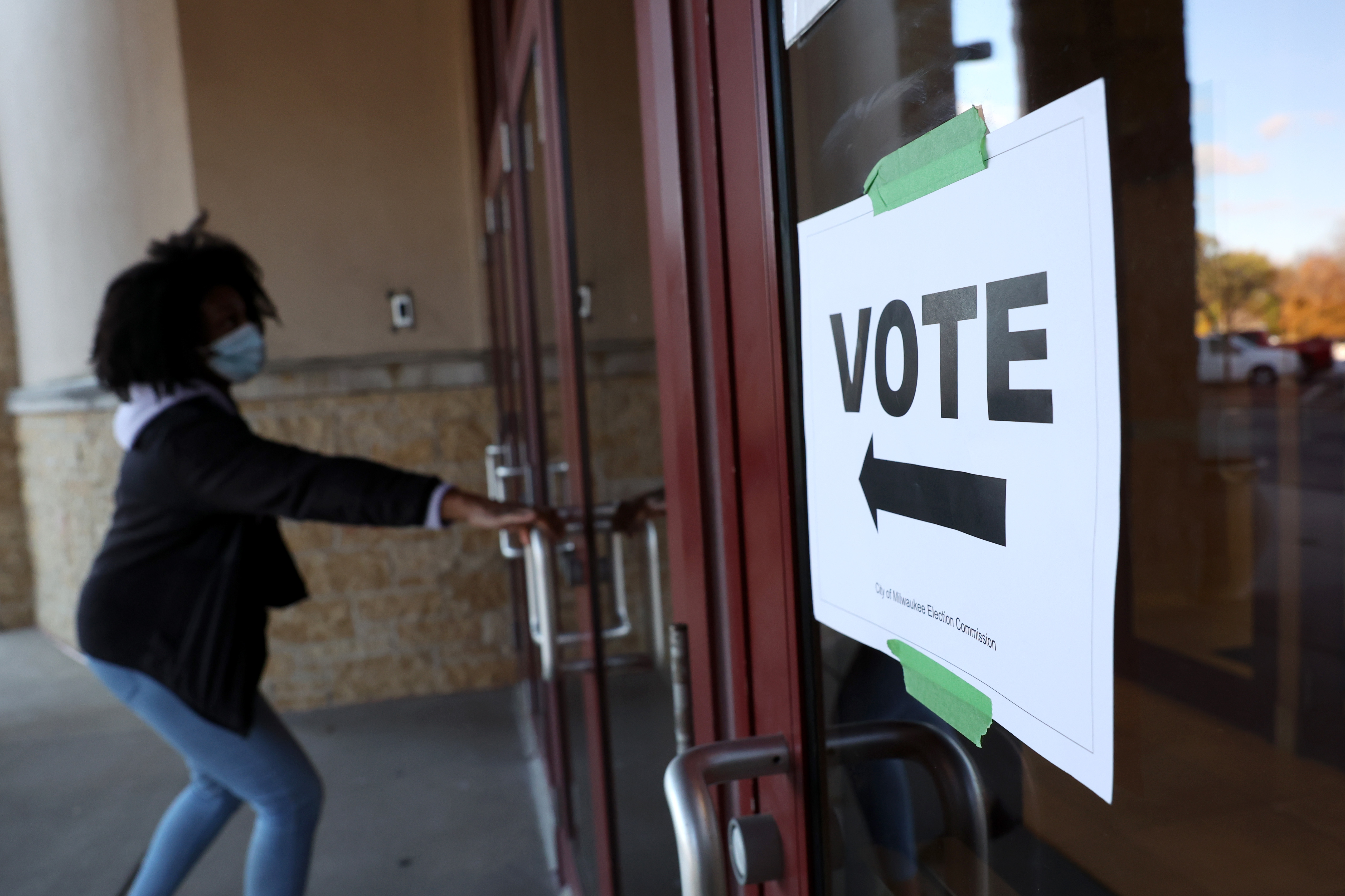 A person pulls open a door beside a sign that reads “vote” and has an arrow pointing left.
