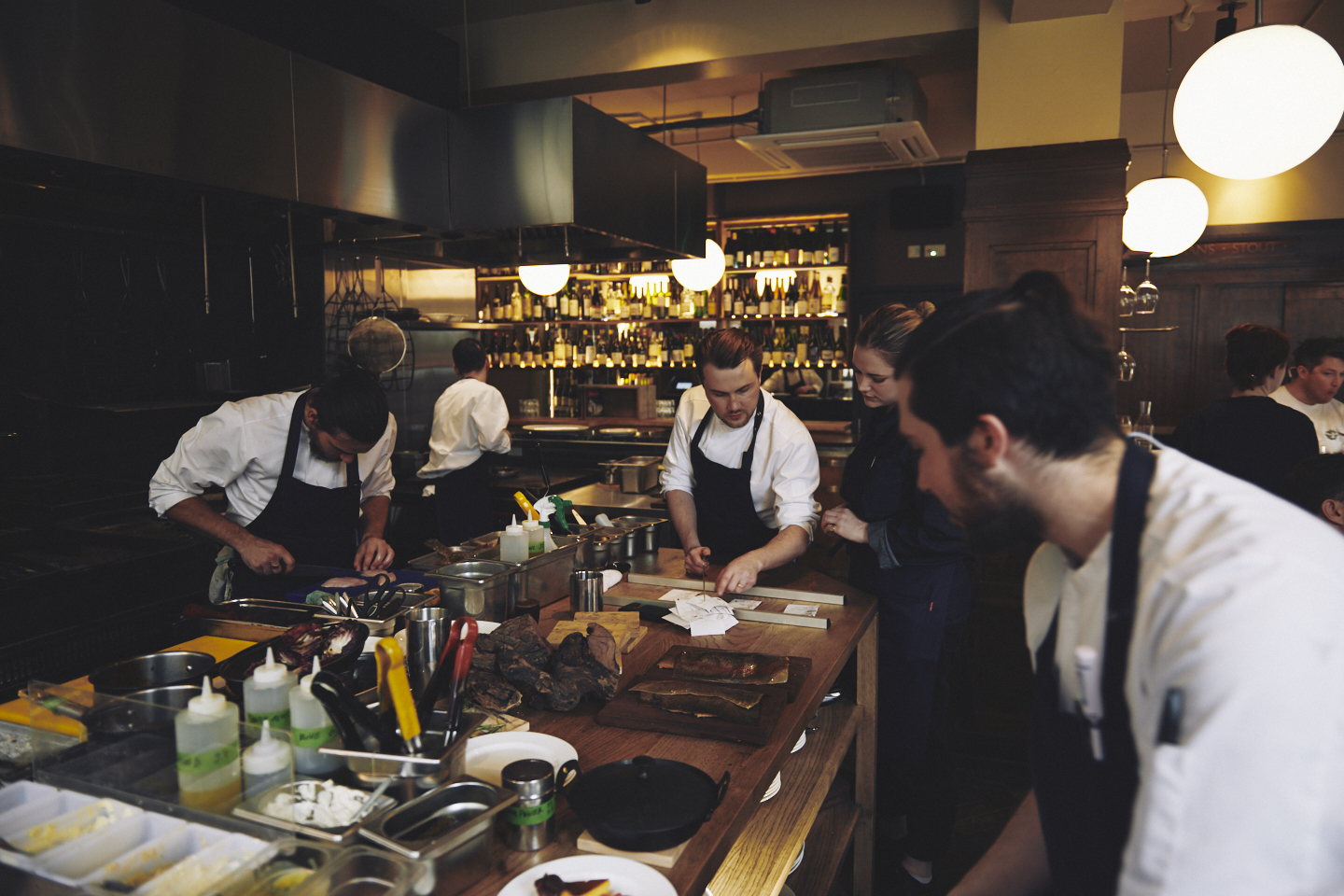 Chefs stand and work in blue aprons and whites at the pass at Brat restaurant Shoreditch