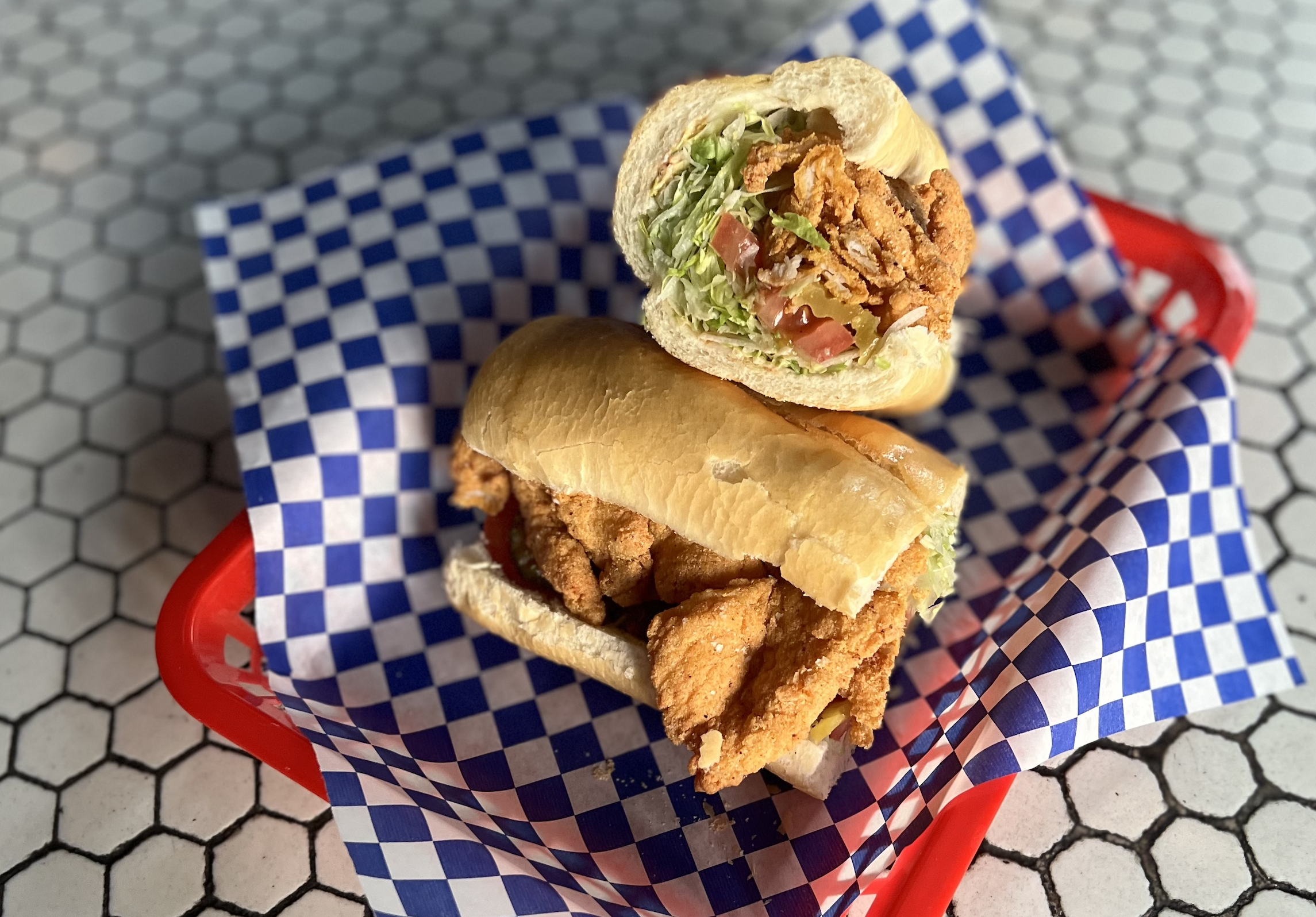A catfish po’ boy from Lollipop Shoppe arrives cut in half in a red basket, lined with blue-and-white paper.