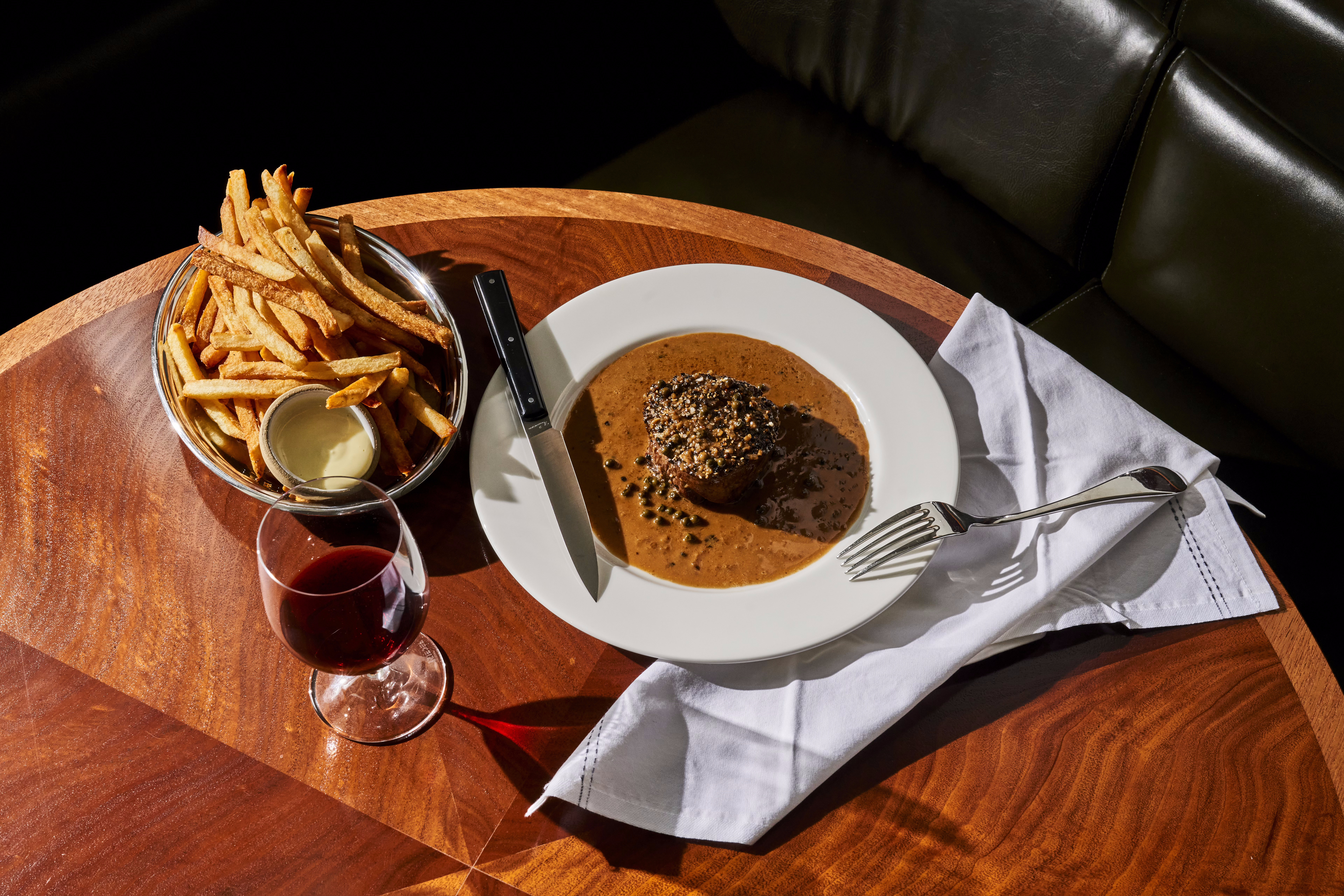 Bison au poivre sits on a plate, slathered in orange cream peppercorn sauce; a plate of fries sit on the side.