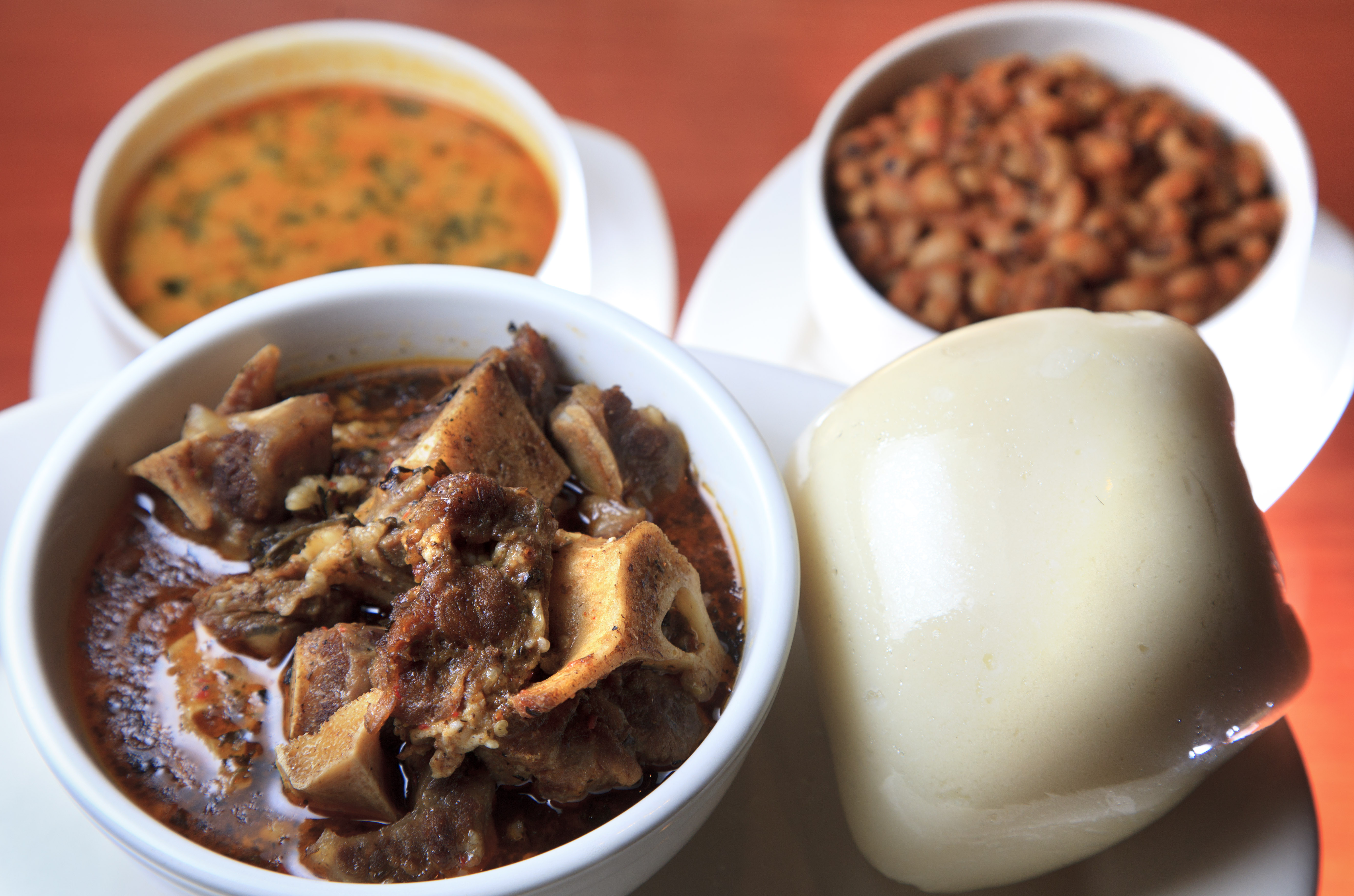 The oxtail pepper stew is shown with pounded yam fufu, at right, taushe (peanut soup) at back left, and stewed black eyed peas, back right. Suya Joint is a restaurant in Roxbury that serves traditional Nigerian cuisine.