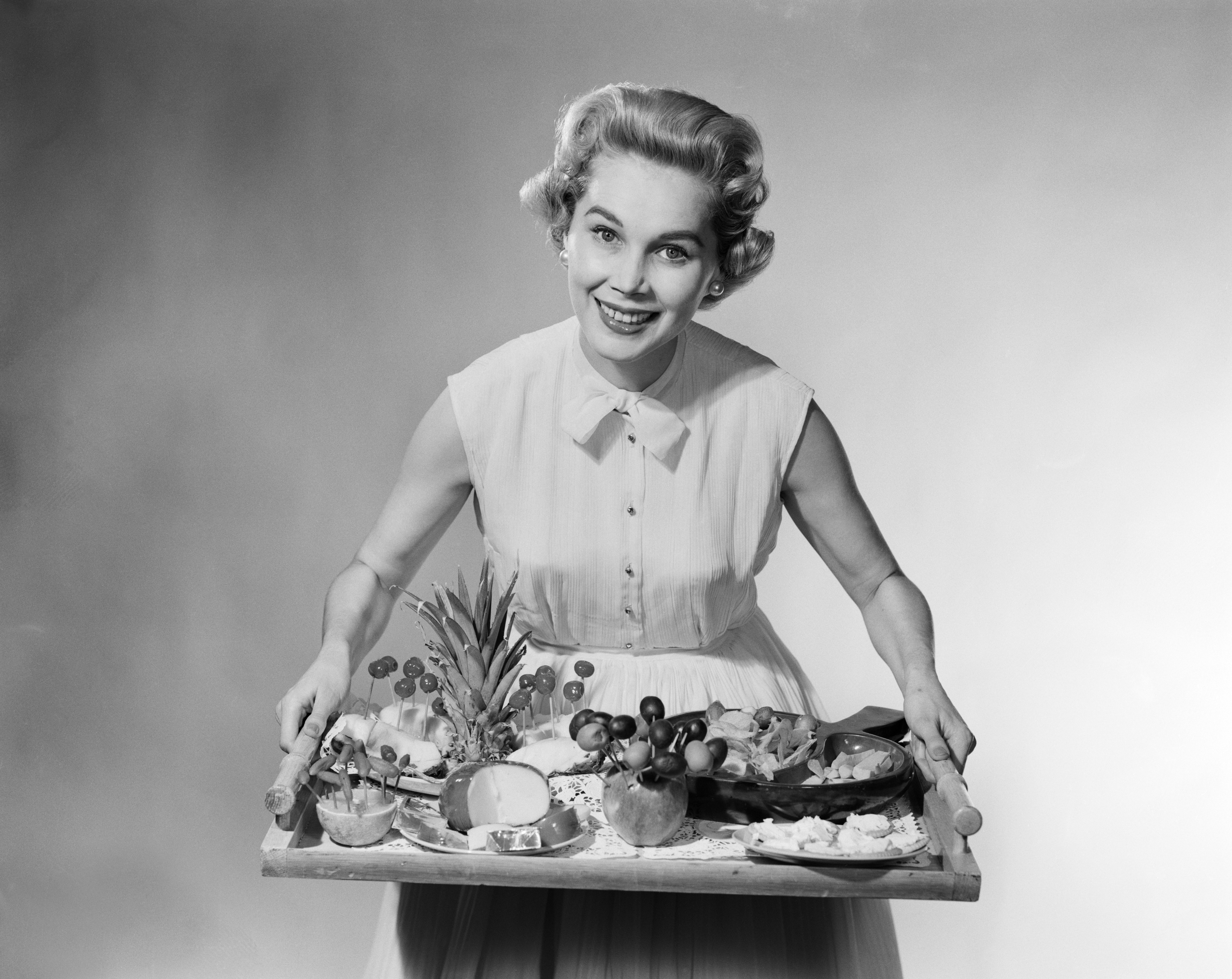 A black and white photo of a woman holding a tray of food