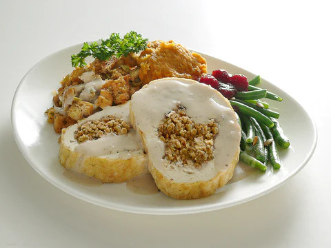 A meat-free Thanksgiving meal on a plate with a veggie roast that looks like a turkey breast with stuffing.