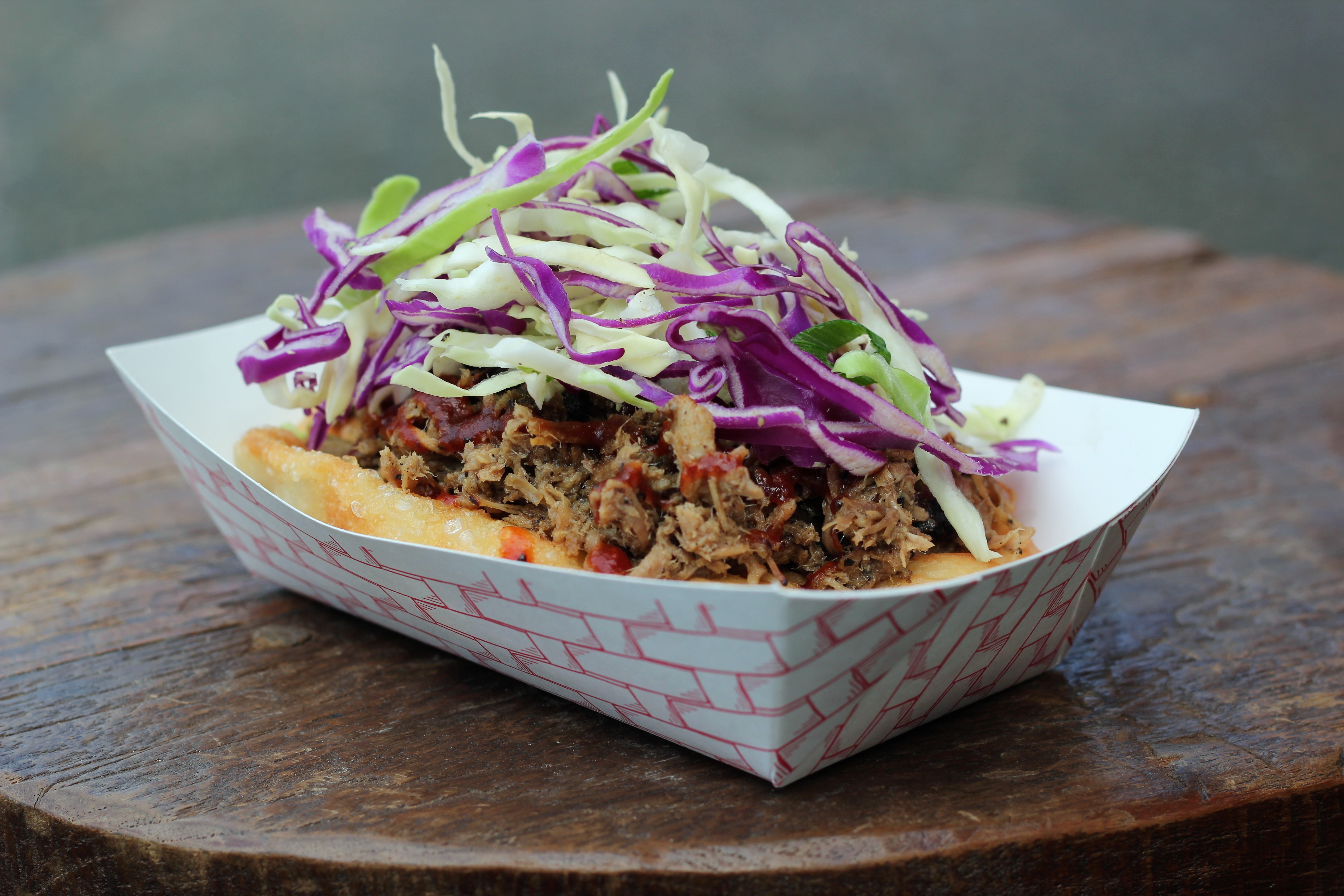 A closeup view of a pile of Off the Rez Cafe’s pulled pork fry bread taco inside a paper bowl, topped with coleslaw.
