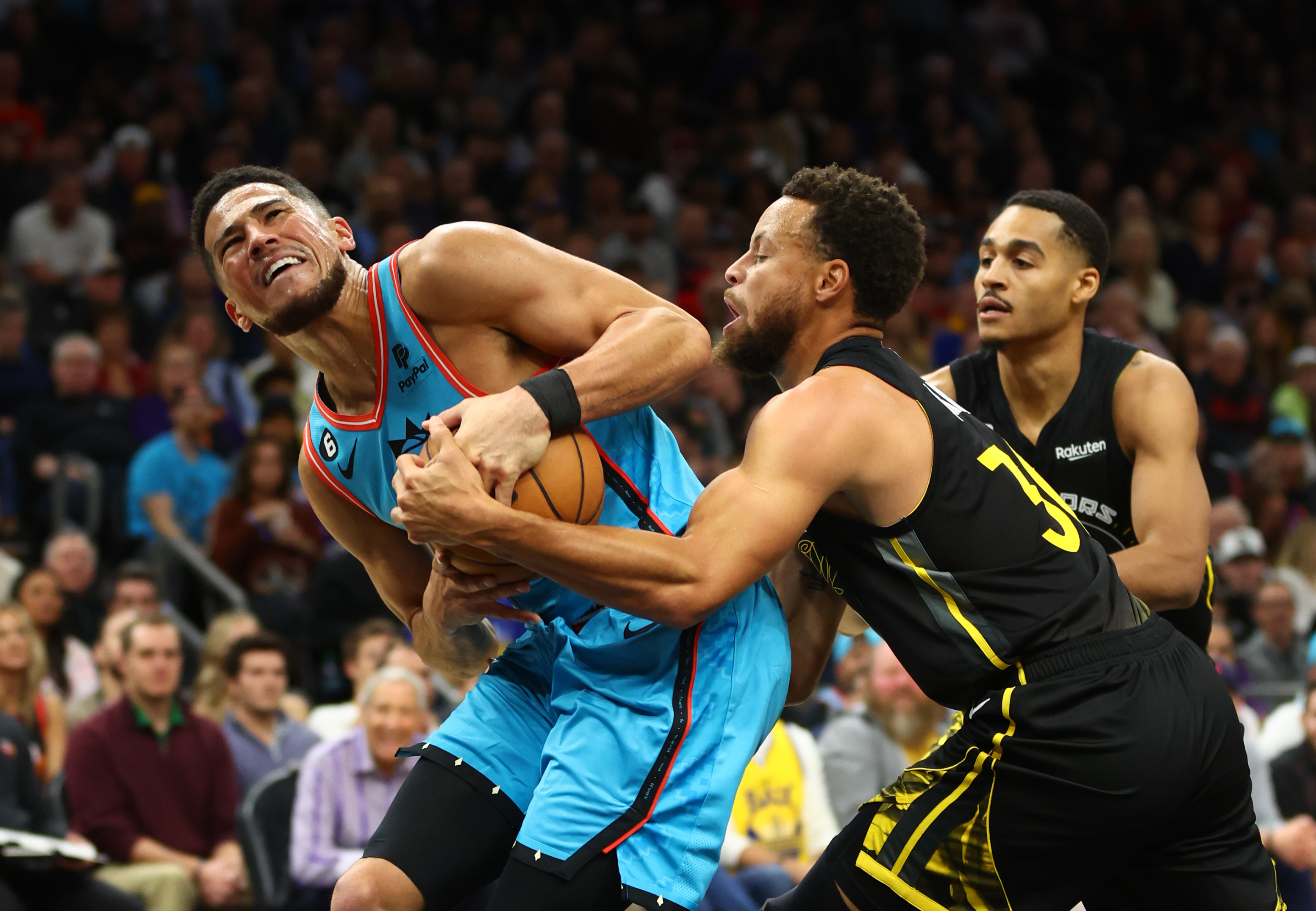 Steph Curry and Devin Booker fighting for the ball with Jordan Poole in the background