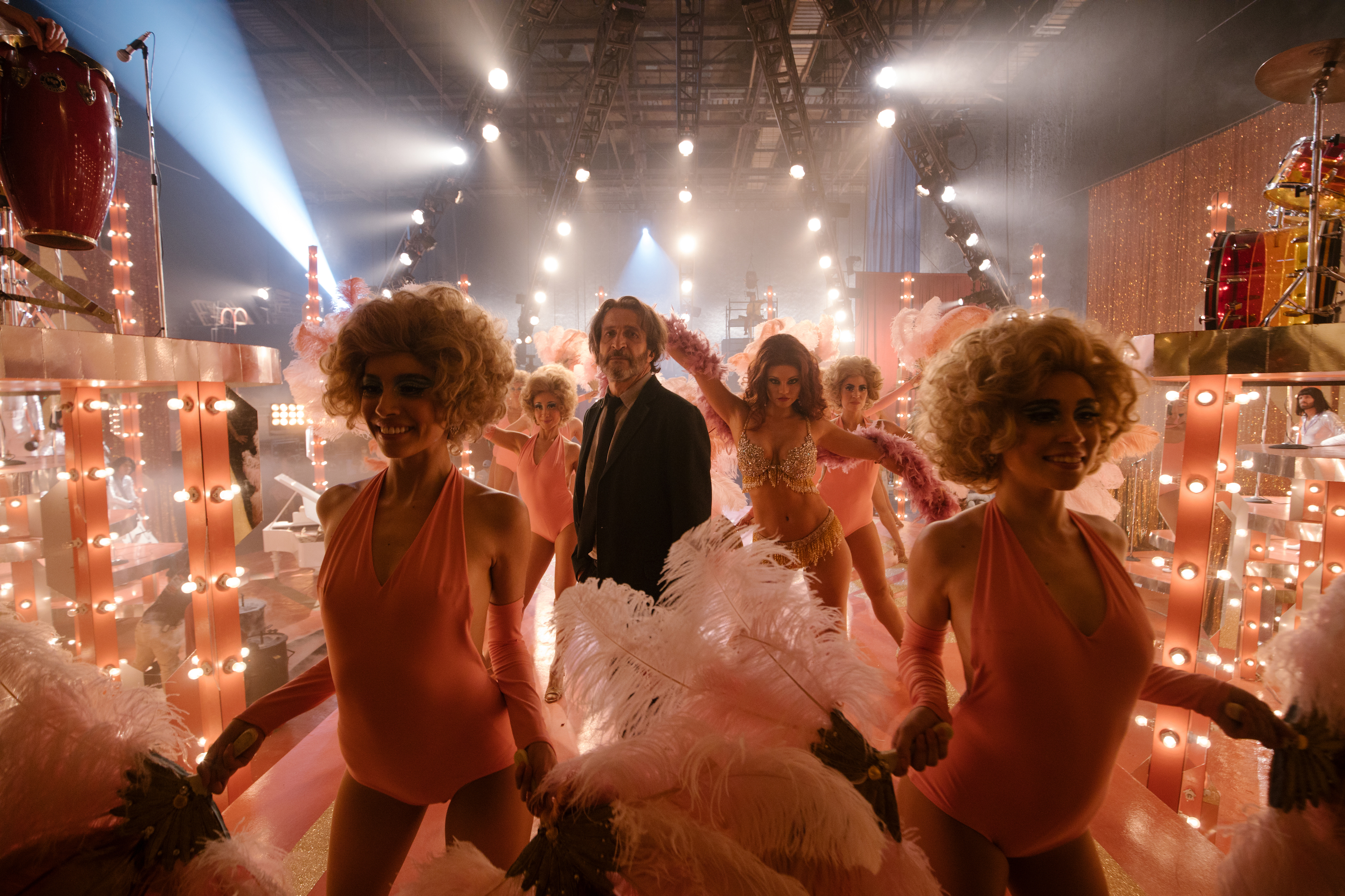 Silverio (Daniel Gimènez Cacho), a salt-and-pepper-bearded man in a plain black suit, stands in the middle of a visual cacophony of dressing-room mirrors and lights, overheard banks of spotlights, and showgirls in blonde curly wigs and peach leotards in a scene from Bardo: A False Chronicle of a Handful of Truths