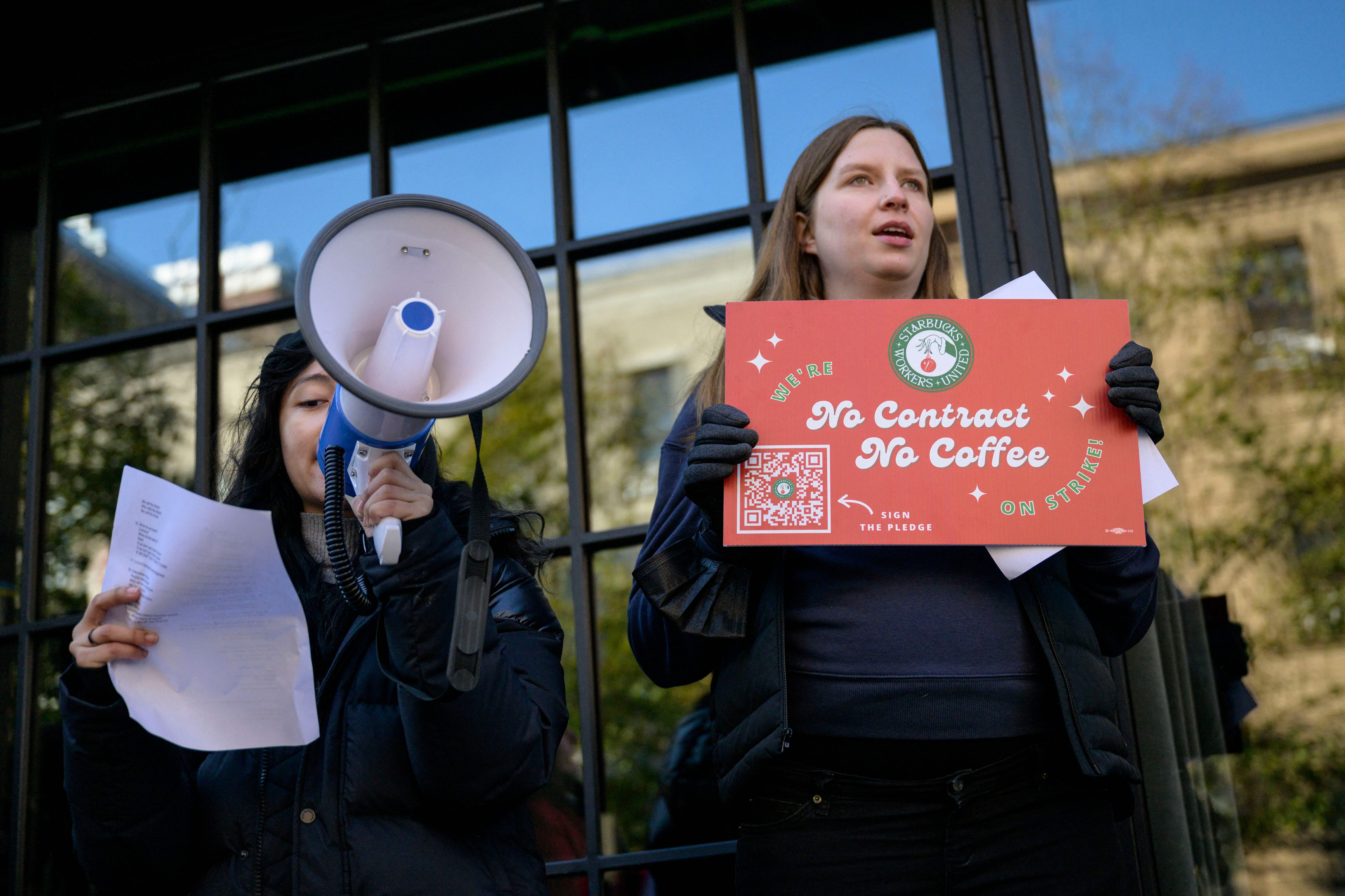 A person holds a bull horn and another holds a sign stating “No Contract, No Coffee.”