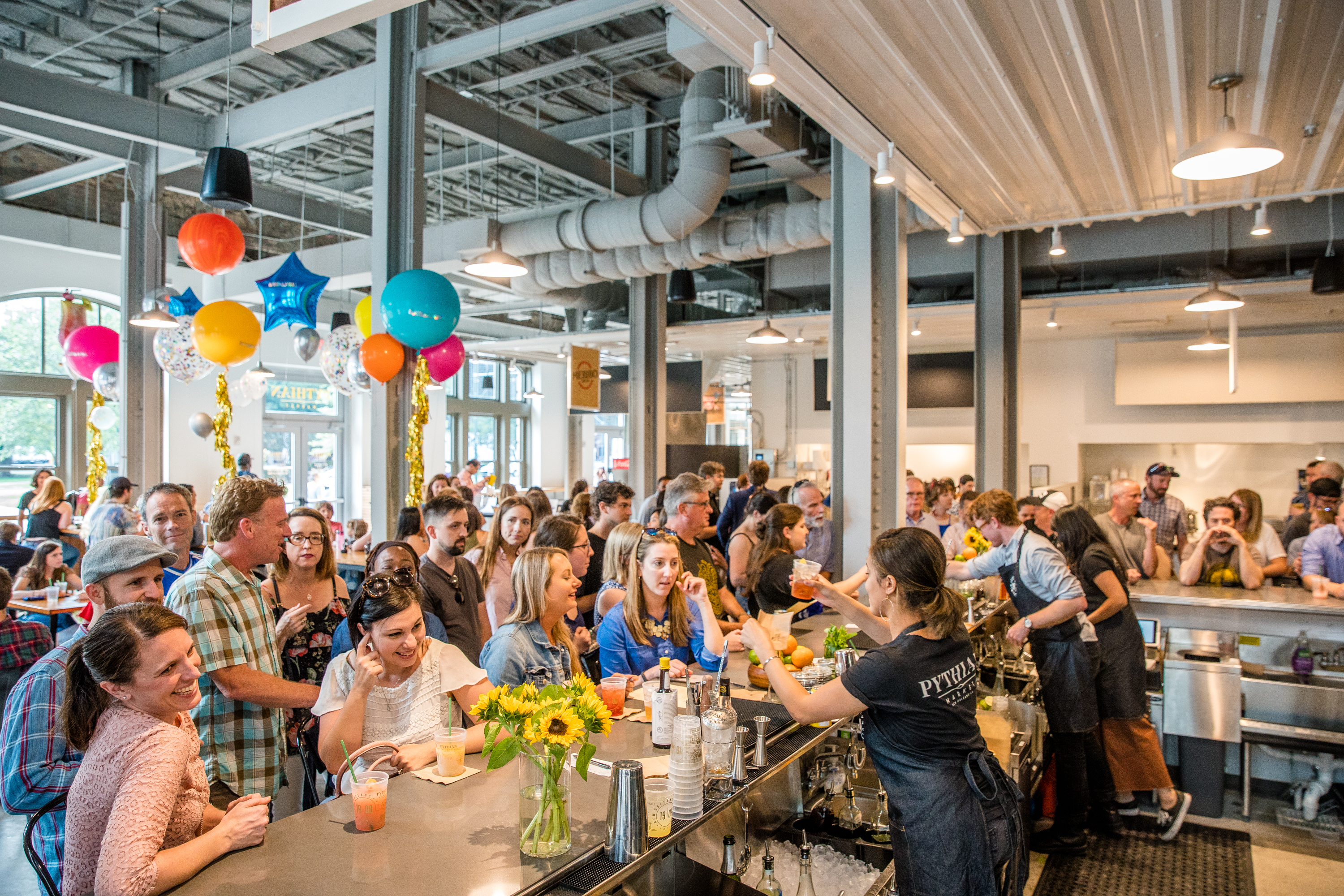 A crowd of people stand at a bar awaiting drinks in a food hall.