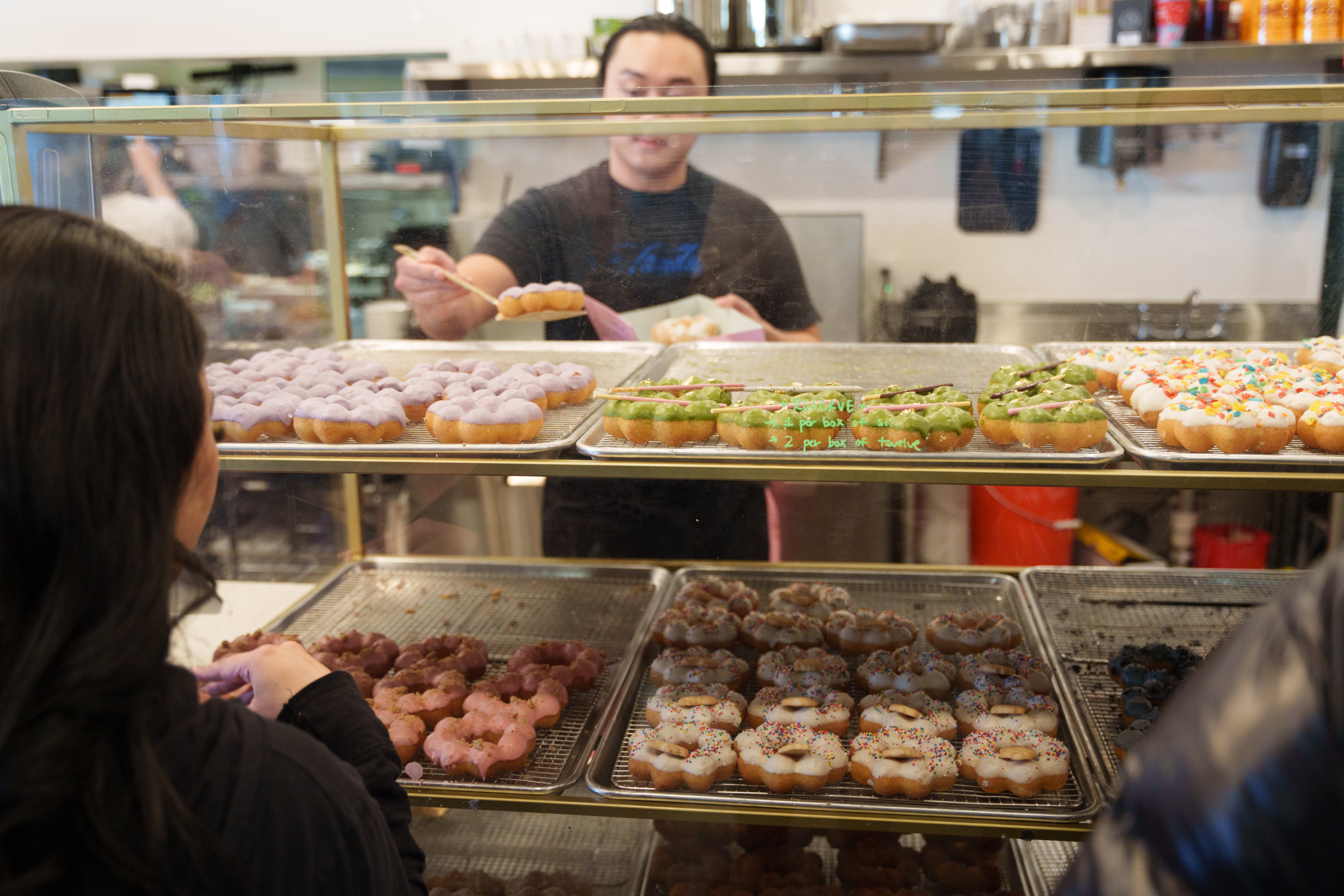 A person grabs a mochi doughnut off a bakery shelf to put it in a box. 