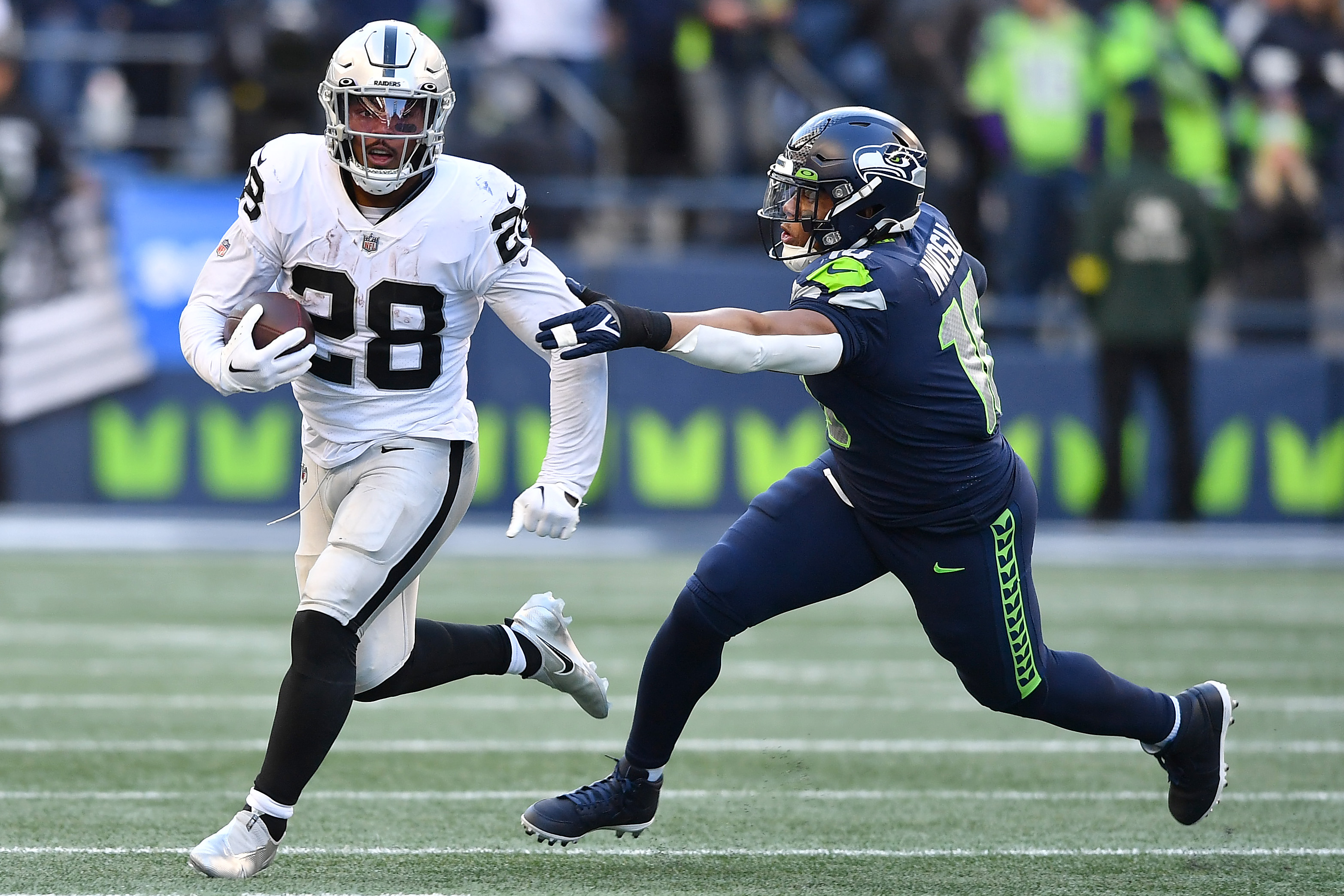 Josh Jacobs #28 of the Las Vegas Raiders runs with the ball while being chased by Uchenna Nwosu #10 of the Seattle Seahawks in the third quarter at Lumen Field on November 27, 2022 in Seattle, Washington.