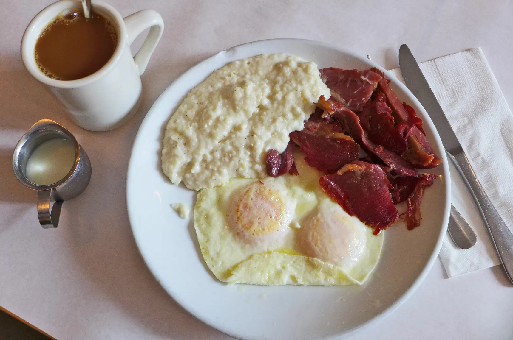 An overhead photograph of a plate of grits, eggs, and bacon.