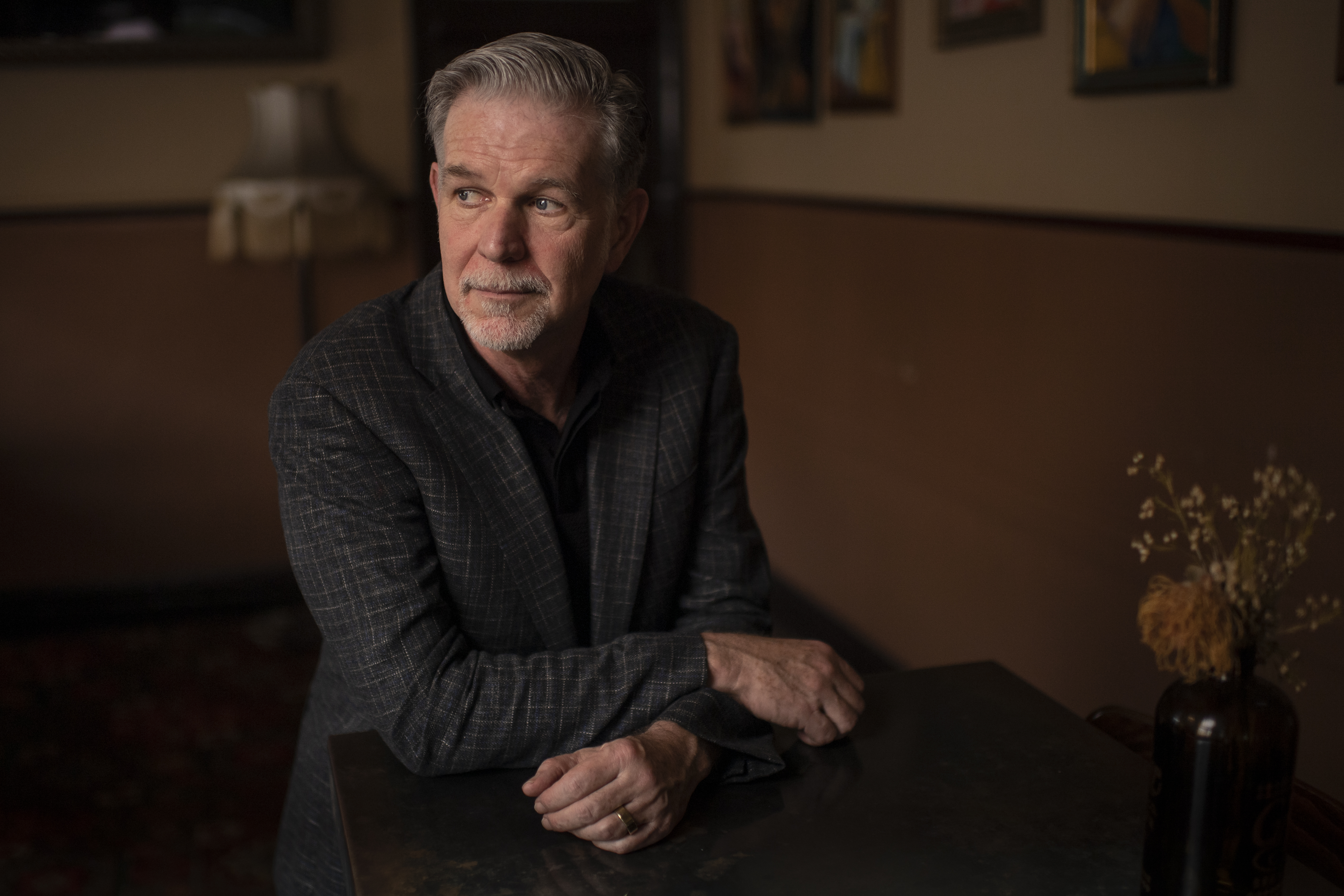 Photo of Reed Hastings, seated and with his arms crossed, looking to the side in a dark room.
