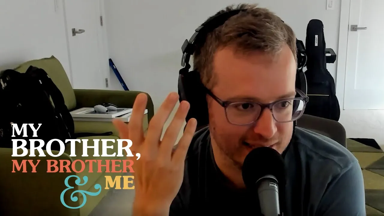 A photo of Griffin in his office, talking into a microphone, with his right hand raised in the air. Superimposed on the lower left corner of the image is the MBMBaM logo.
