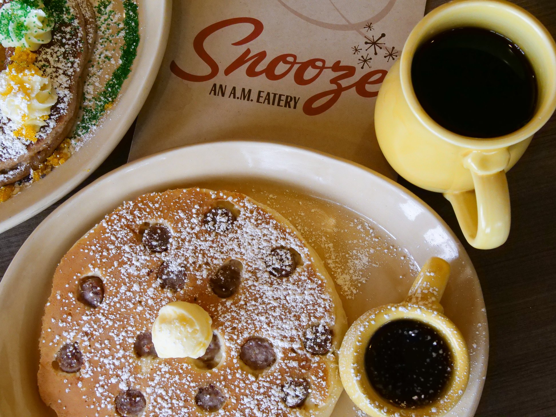 A close-up of a plate of pancakes with butter and syrup next to a cup of coffee at Snooze