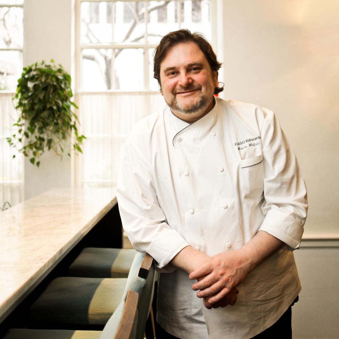 A chef smiling with his arms down wearing white.