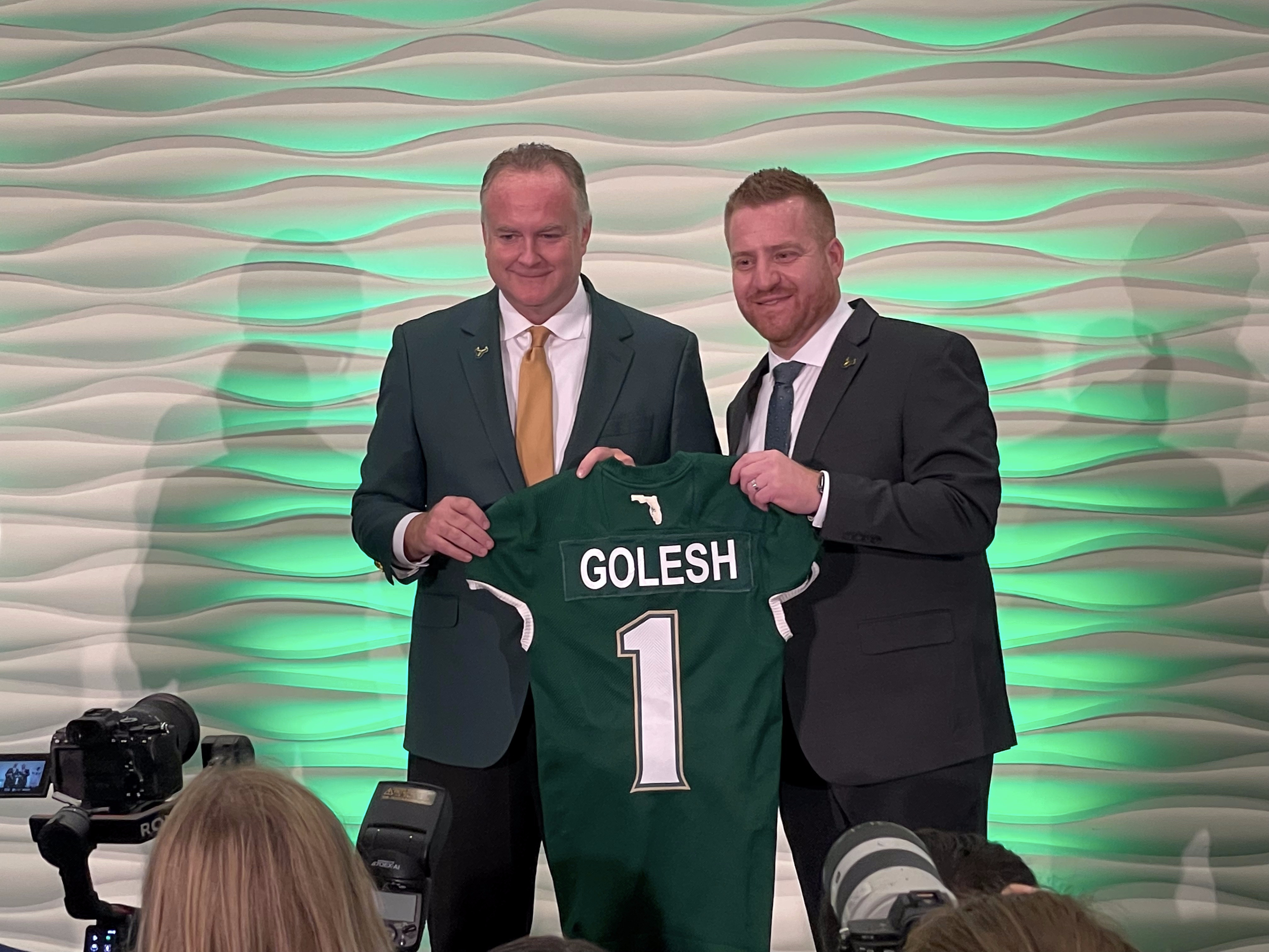 Michael Kelly and Alex Golesh hold up a Golesh USF Football jersey during his introductory press conference. 