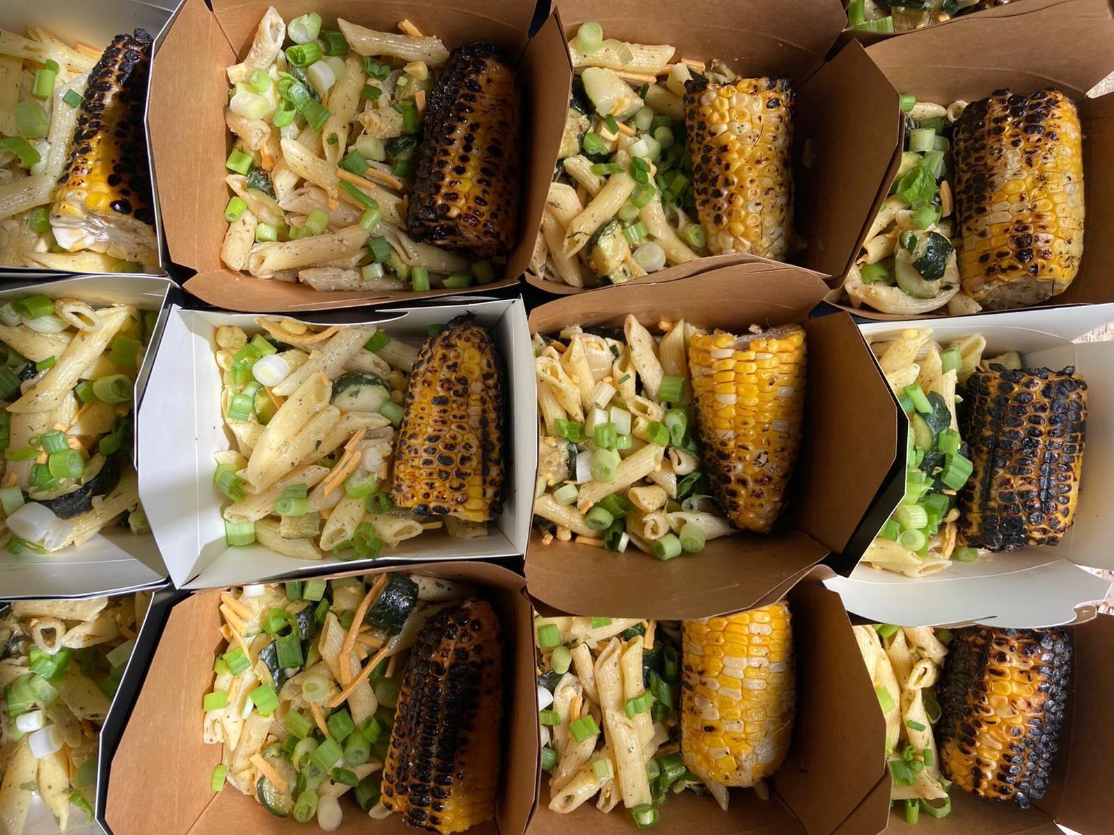Various takeout containers full of pastas and corn.